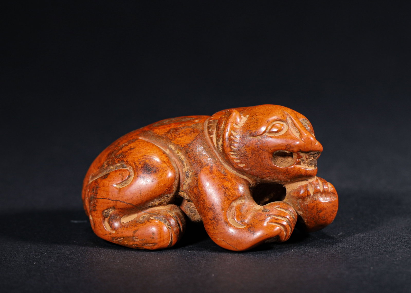 RED AGATE RECUMBENT TIGER PENDANT, HAN DYNASTY (202 BC-220 AD): H 3.4cm (1.34 in); L 7cm (2.76 in); W 4.5cm (1.77 in); Wt 126g (0.28 lb),Carved from red agate with rich crimson tone, marked by mottled patina and natural fissures. Fully modelled recumbent tiger, fr