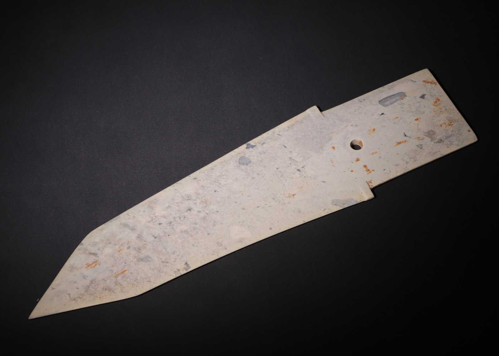 ARCHAIC JADE GE DAGGER-AXE, SHANG DYNASTY (C.1600?C1046 BC): L 36cm (14.17 in); W 9.5cm (3.74 in); Wt 352g (0.78 lb),The jade is overall calcified and suffused with greyish-white patina, scattered with orange-brown soil stains. Elongated flat form with a long b