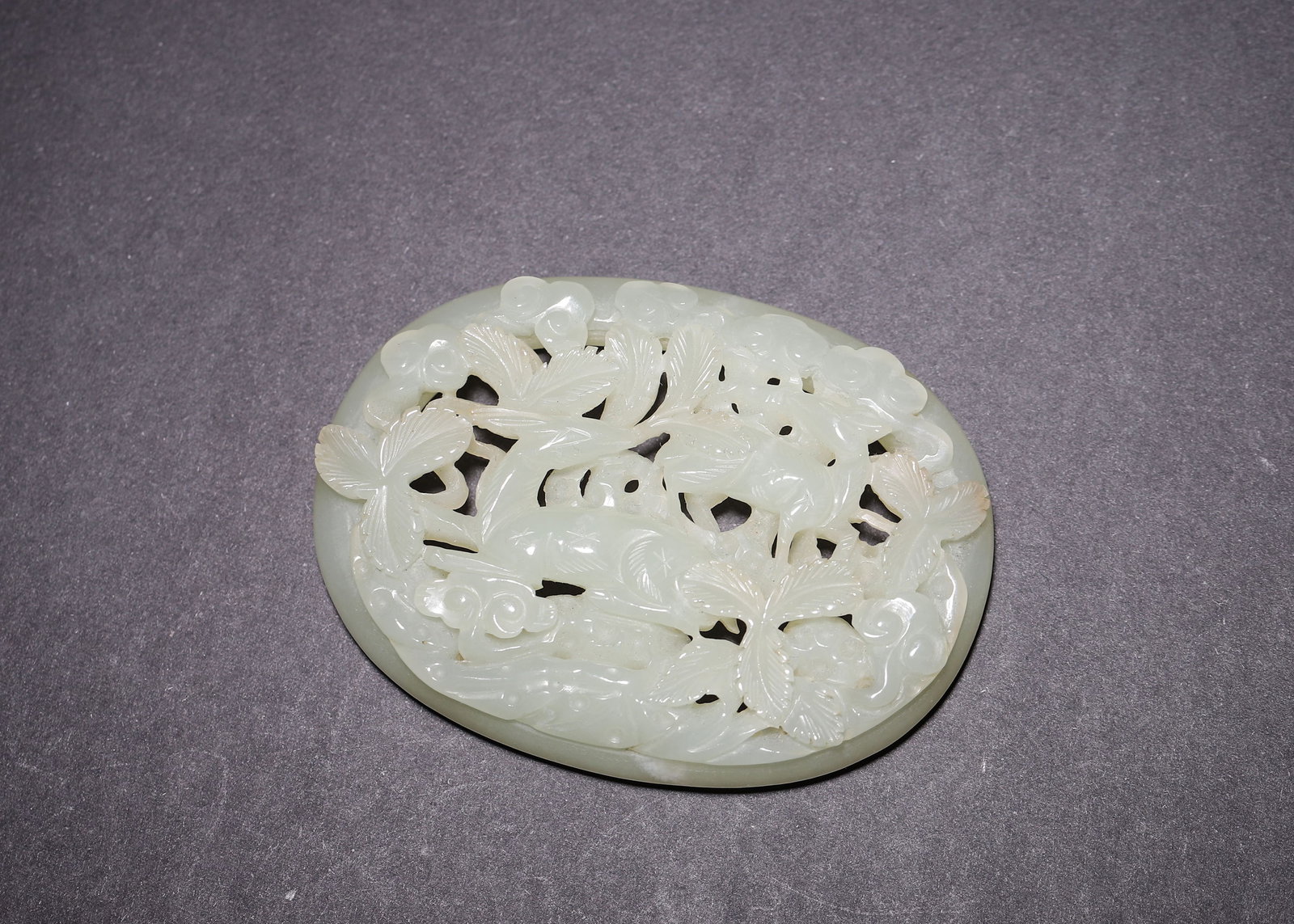 QING DYNASTY PALE CELADON HETIAN JADE OPENWORK BELT PLAQUE WITH TWIN DEER, PINE AND CLOUD MOTIFS,: L 8.00cm (3.15 in); W 6.00cm (2.36 in); Wt 71.00g (0.16 lb),Oval framed belt plaque carved from pale celadon Hetian jade. Obverse multi-layer openwork of twin deer, pine and scroll clouds, fine incise