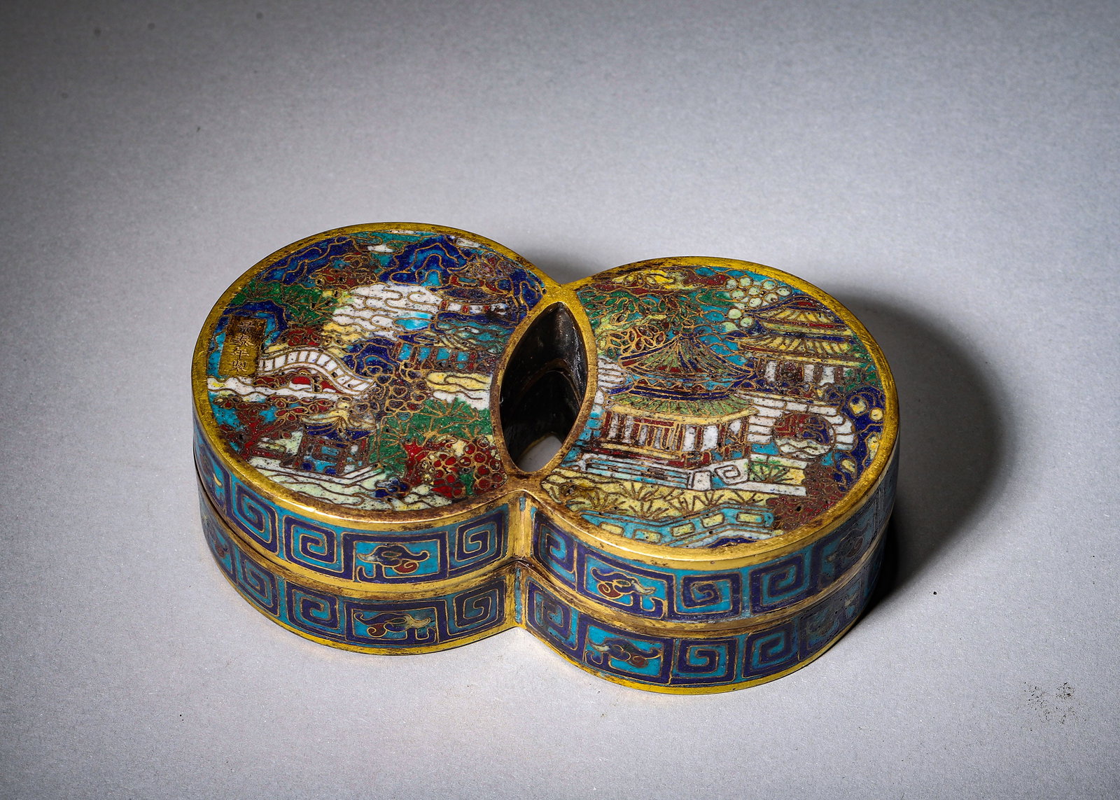 GILT COPPER-BODY CLOISONNE DOUBLE-LOBED LIDDED BOX WITH LANDSCAPE PAVILION MOTIFS, JINGTAI MARK: L 12.00cm (4.72 in); W 7.00cm (2.76 in); H 3.50cm (1.38 in); Wt 405.00g (0.89 lb),Gilt copper cloisonne double-lobed ink paste box with gilded border. The lid is divided into two scenic panels painted