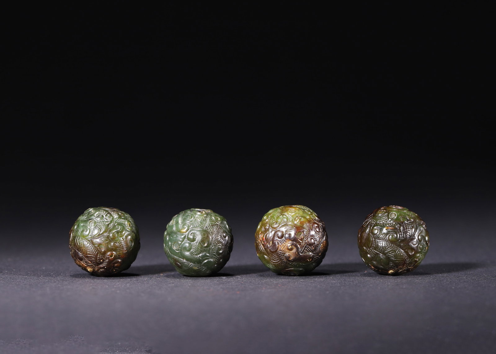 A SET OF FOUR HETIAN GREEN JADE BEADS WITH HIGH-RELIEF DRAGON, PHOENIX AND AUSPICIOUS BEAST MOTIFS,: D 2.20cm (0.87 in); Wt 59.00g (0.13 lb),Carved from Hetian green jade, fully suffused with layered russet ancient patina. Each bead fully covered in high-relief interwoven dragon, phoenix and chilong 
