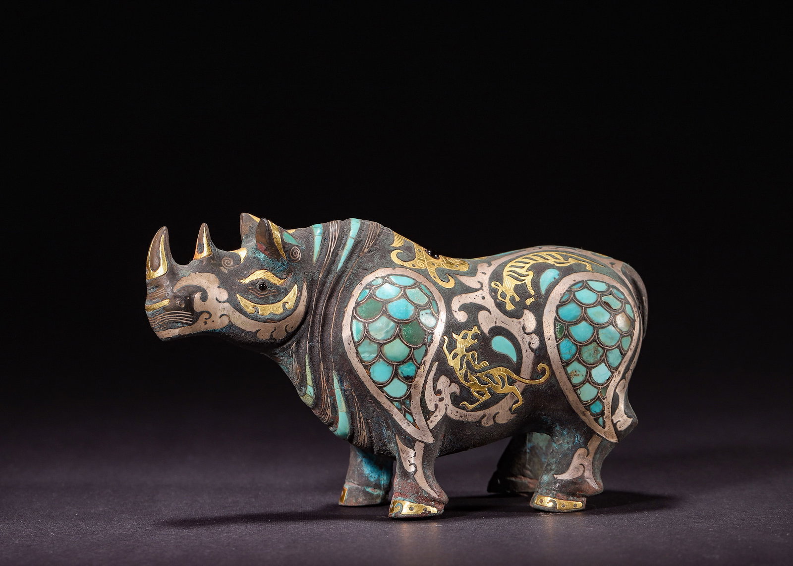 GOLD AND SILVER INLAID BRONZE RHINOCEROS ZUN WITH TURQUOISE, HAN DYNASTY (206 BC?C220 AD): H 8cm (3.15 in); L 14cm (5.51 in); W 5cm (1.97 in); Wt 505g (1.11 lb),Bronze rhinoceros-form zun vessel, inlaid with gold, silver and turquoise scales, interspersed with feline motifs. Robust figure, 