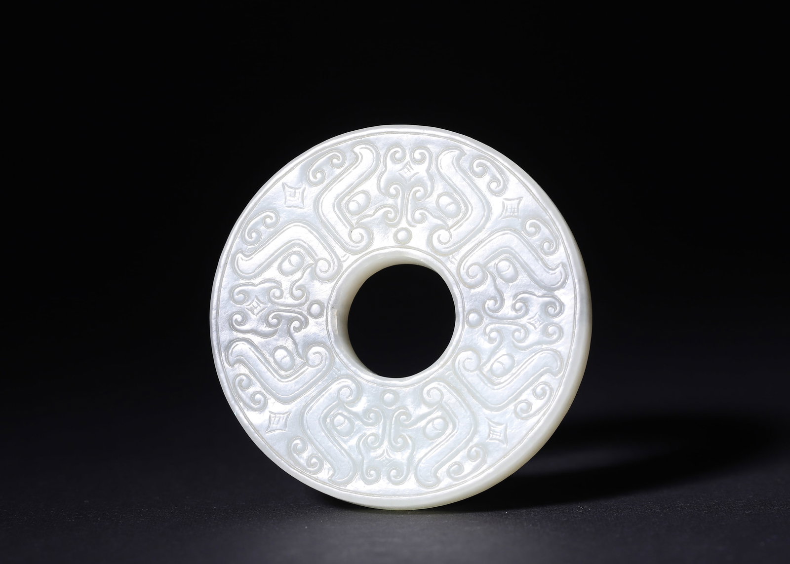 QING DYNASTY WHITE HETIAN JADE BI DISC WITH DOUBLE-SIDED RELIEF AUSPICIOUS BEASTS AND CLOUD SCROLLS,: D 5.60cm (2.20 in); Wt 54.00g (0.12 lb),Standard circular jade bi disc of white Hetian jade, well-proportioned central aperture and outer band, solid thickness. One side carved with six symmetrical ar