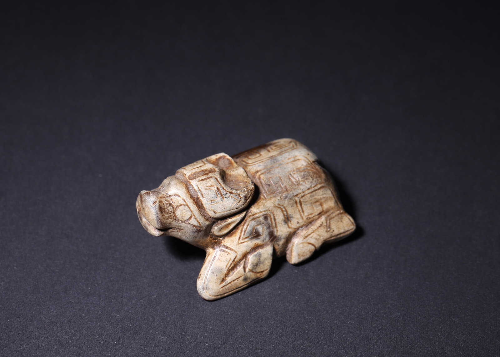 LATE SHANG DYNASTY CALCIFIED JADE RECUMBENT OX PENDANT, C.11TH?C10TH CENTURY BCE: L 5.50cm (2.17 in); W 3.70cm (1.46 in); H 2.50cm (0.98 in); Wt 61.00g (0.13 lb),Solid carved jade recumbent ox, heavily calcified to pale grey-white with residual russet native jade. Classic Shang dou
