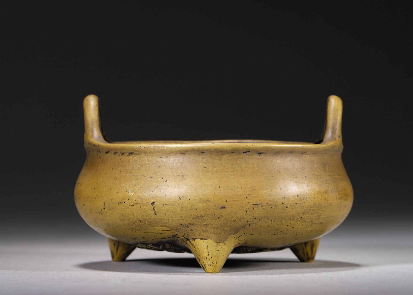 MING DYNASTY BRONZE TRIPOD CENSER WITH UPRIGHT LOOP HANDLES, TWIN DRAGON RELIEF AND MARK "DA MING: D 10cm (3.94 in); H 6cm (2.36 in); Wt 344g (0.76 lb),Cast from fine bronze, the censer features a squat rounded body, upright loop handles and three pointed mammiform feet. It bears smooth warm eel-ye