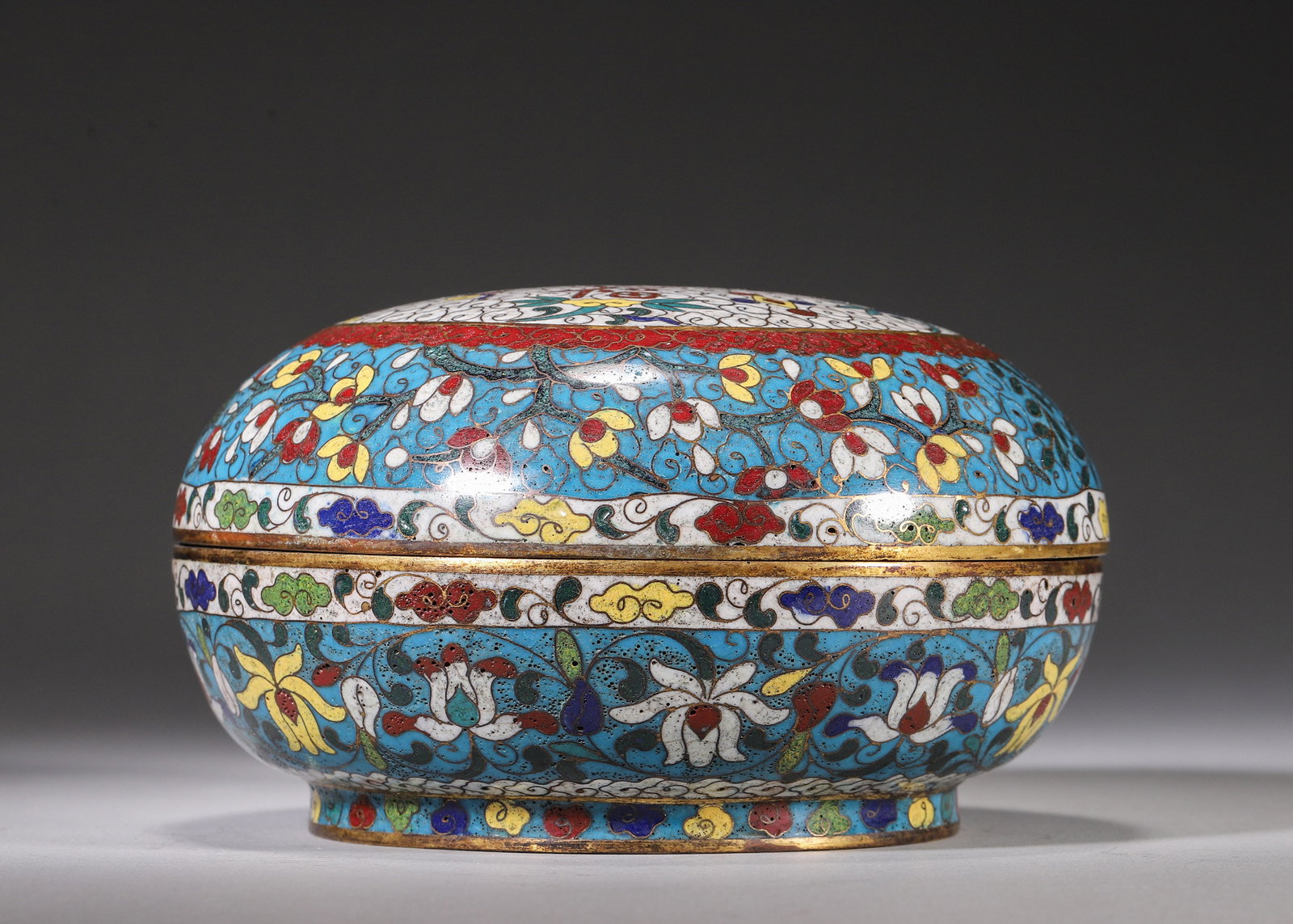 COPPER-BODY CLOISONNE CIRCULAR LIDDED BOX WITH MAGNOLIA FLORAL MOTIFS, WANLI MARK: H 8.00cm (3.15 in); D 16.00cm (6.30 in); Wt 878.00g (1.94 lb),Round copper cloisonne ink paste box on turquoise enamel ground with elaborate gilded wire floral scrolls. The lid bears four auspicious c