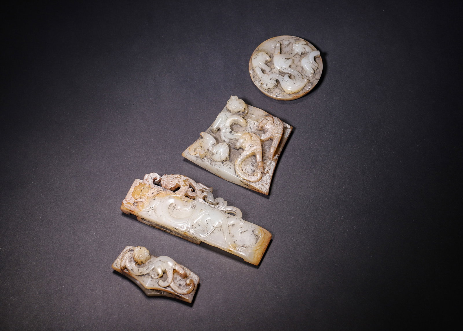 A COMPLETE SET OF FOUR HETIAN WHITE JADE SWORD FITTINGS WITH HIGH-RELIEF CHILONG DRAGONS, HAN: L 11.20cm (4.41 in); W 4.20cm (1.65 in); Wt 349.00g (0.77 lb),Carved from Hetian white jade with smooth texture, fully covered in earthy yellow and black burial patina. A complete four-piece set: pomm