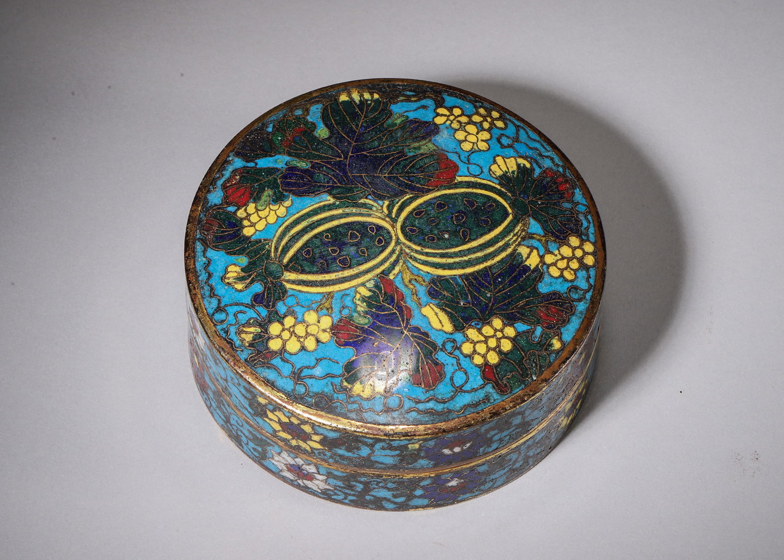 COPPER-BODY CLOISONNE CIRCULAR LIDDED BOX WITH MELON AND GRAPE MOTIFS, MARKED WANLI MARK: H 5.00cm (1.97 in); D 12.00cm (4.72 in); Wt 550.00g (1.21 lb),Round copper cloisonne ink paste box with turquoise enamel ground outlined by gilded copper wires. The lid is decorated with twin melons a