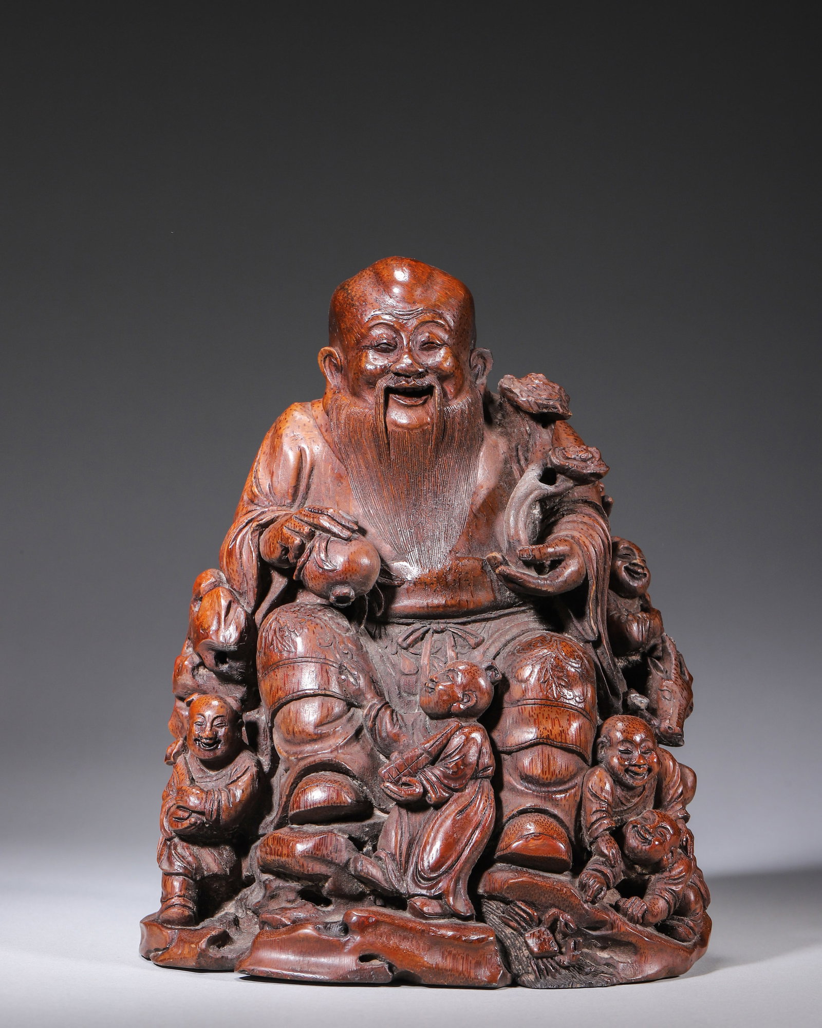 QING DYNASTY BAMBOO ROOT CARVED GOD OF LONGEVITY WITH NINE BOYS, SIGNED TIANZHANG: L 16.00cm (6.30 in); W 13.00cm (5.12 in); H 20.00cm (7.87 in); Wt 632.00g (1.39 lb),Carved from a single aged bamboo root with antique reddish-brown patina. The God of Longevity holds a peach and ling