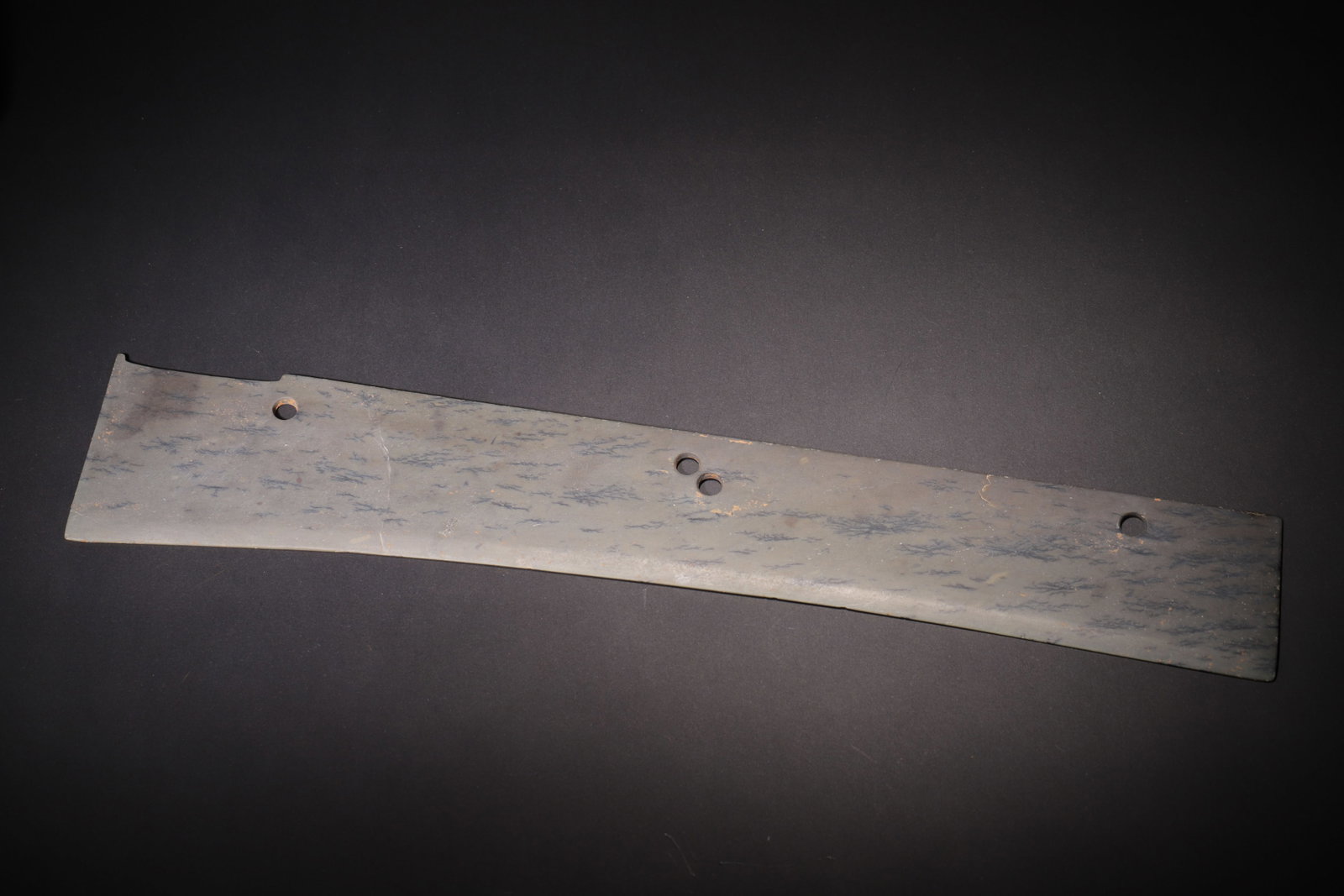FOUR-HOLE JADE KNIFE, SHANG DYNASTY (C.1600?C1046 BC): L 46cm (18.11 in); W 8cm (3.15 in); Wt 369g (0.81 lb),Carved from green jade naturally mottled with dendritic inclusions and orange-yellow burial stains. Elongated flat curved knife form with straight