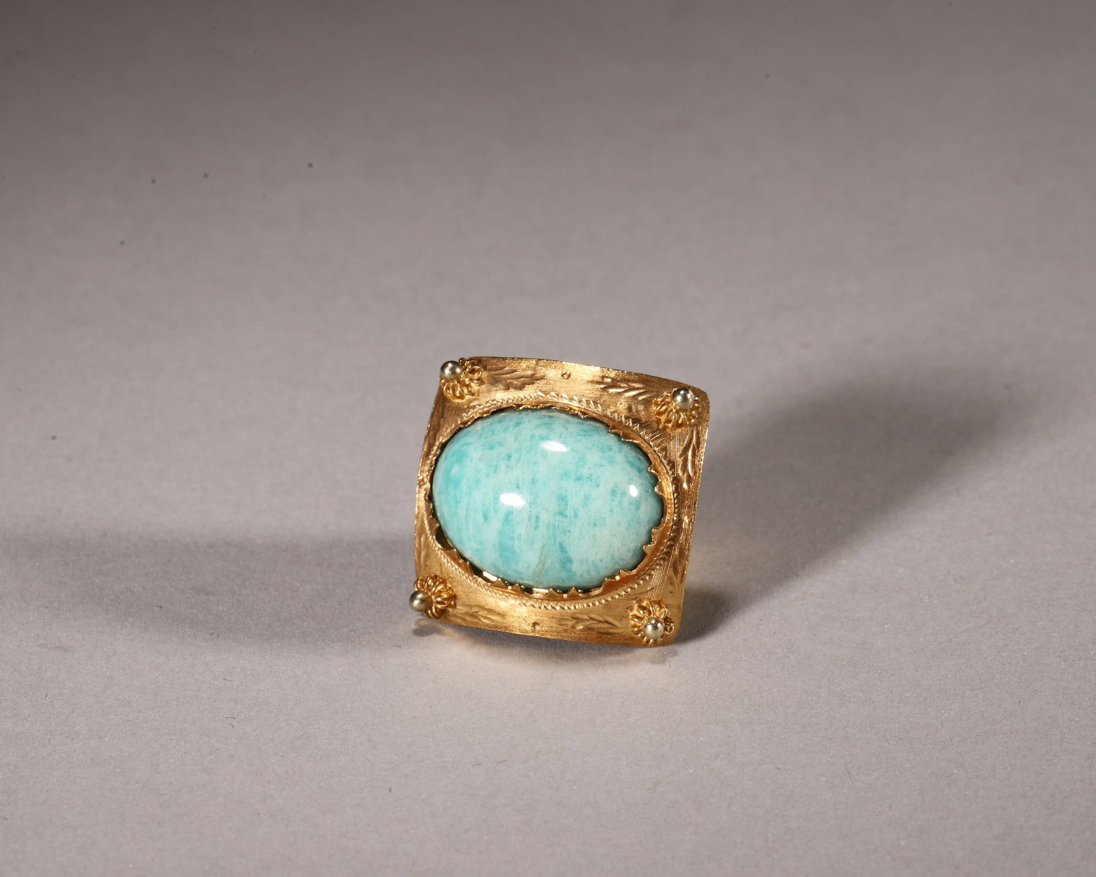 A Hand Chased K Gold Amazonite Pendant: L 2.4cm (0.94 in); W 2.3cm (0.91 in); Wt 11g (0.39 oz)Crafted of K gold with hand chased leaf patterns, this pendant features a cabochon natural amazonite with vivid cyan veining. Four corner bead det