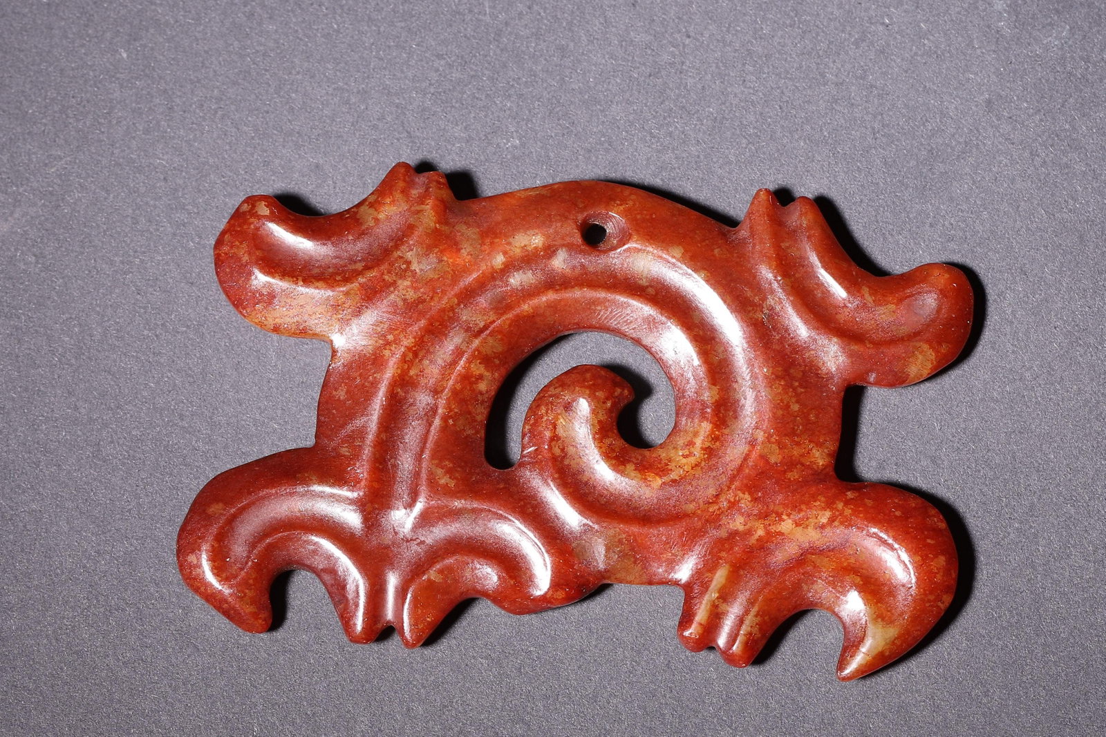 Hongshan Culture, Cloud Shaped Openwork Jade Pendant: Wt 54g (0.12 lb); L 9cm (3.54 in); W 5.7cm (2.24 in)Red brown suffused jade cloud shaped pendant, openwork and relief carving with suspension hole, characteristic Hongshan ritual jade.