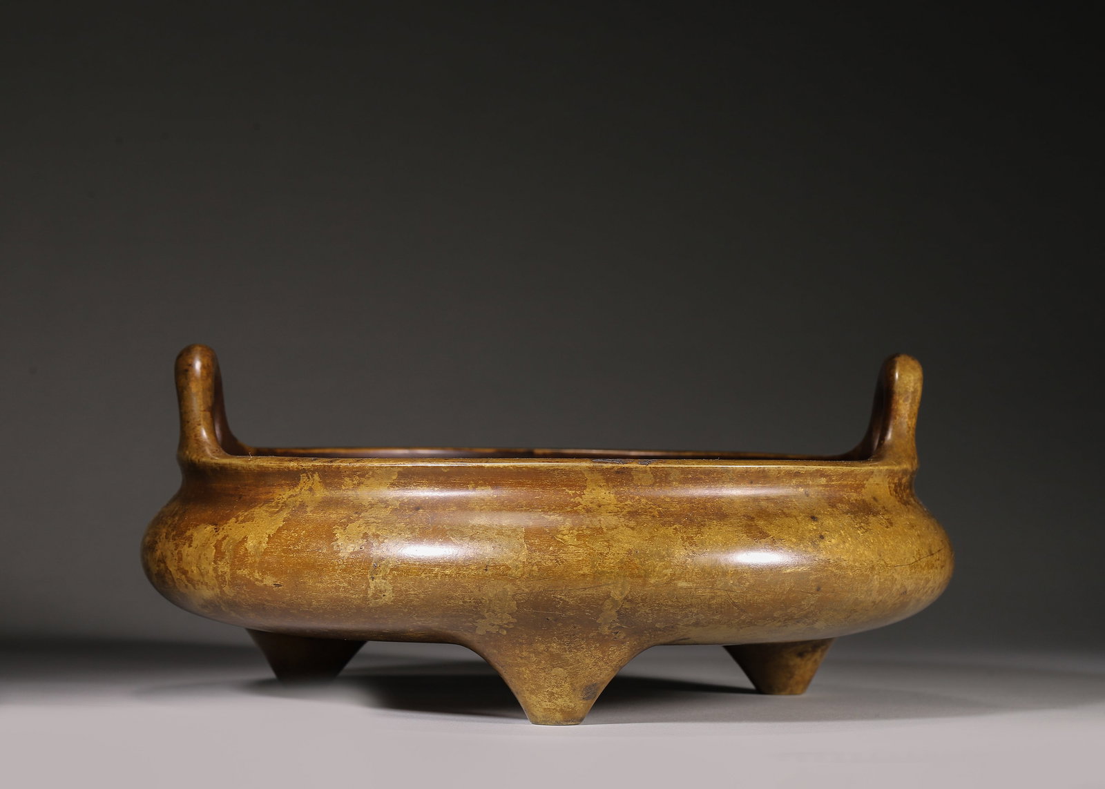 Bronze Tripod Censer With Gilt Splash And Upright Handles (Qing Dynasty,1644 1912): Wt 5145g (11.34 lb),D 28cm (11.024 in),H 12cm (4.72 in)Well cast bronze censer with upright handles, compressed rounded body supported by three feet. Scattered gilt splash across surface with mellow a