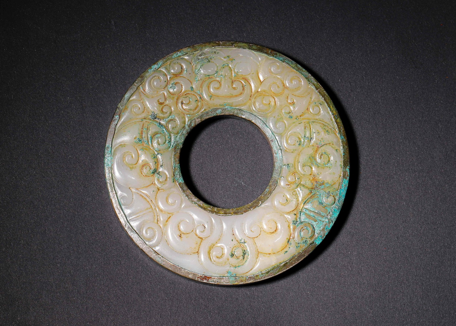 White Jade Bi With Bronze Mounted Cloud Scrolls, Warring States,C.475 221 Bc: Wt 184g (0.41 lb); D 10cm (3.94 in)Bronze mounted on inner and outer rims, both sides finely carved with cloud scrolls. Surface covered with bronze green patina, an elegant Warring States ritual jade.