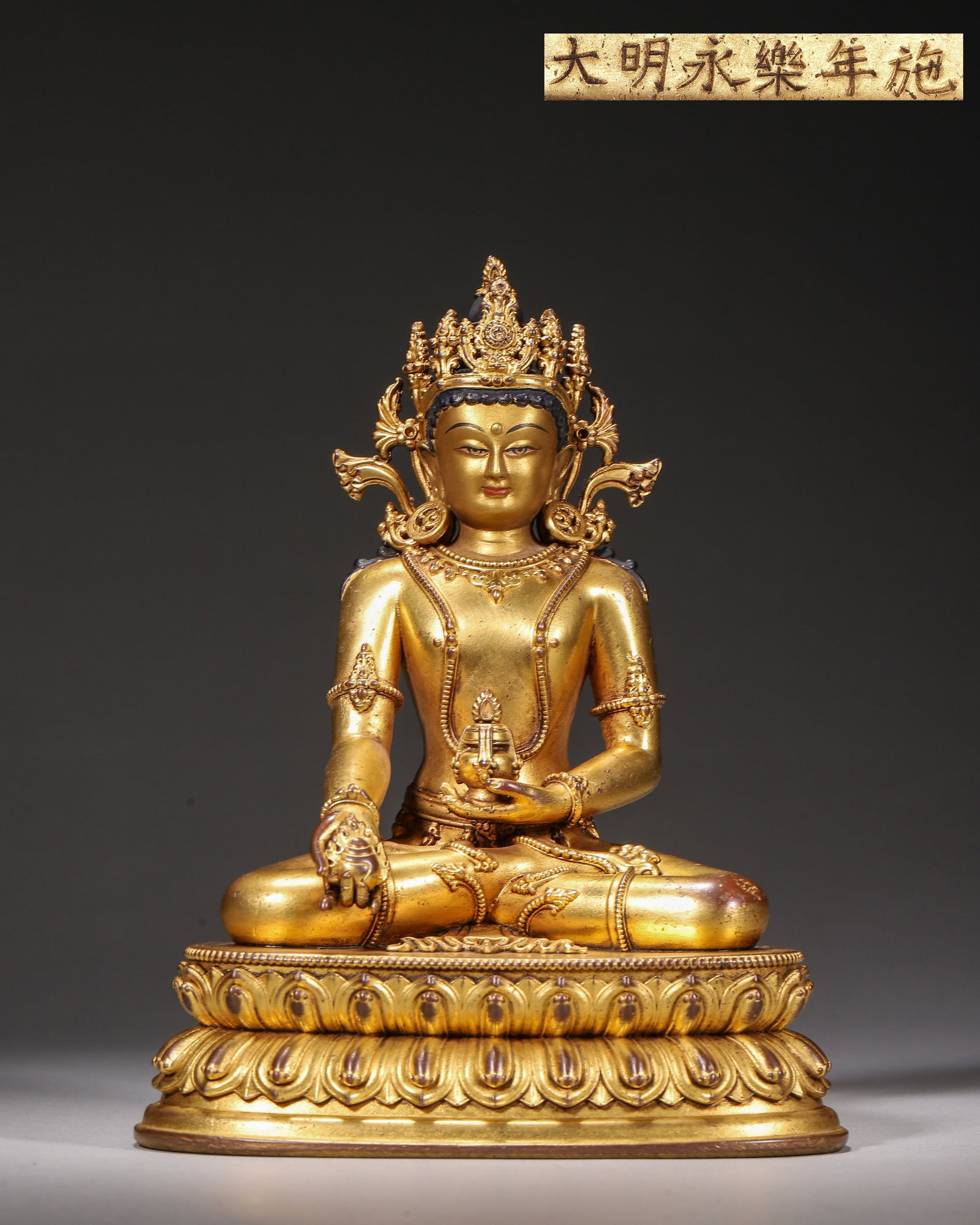 Gilt Bronze Seated Medicine Buddha, Imperial Court Made,Marked "Made In Yongle Reign Of Great: Wt 856g (1.89 lb),L 12cm (4.72 in),W 10cm (3.94 in),H 16cm (6.299 in)Imperial court made.The Buddha sits in padmasana with crown and jewelled adornments. Right hand holds myrobalan in varada mudra, le