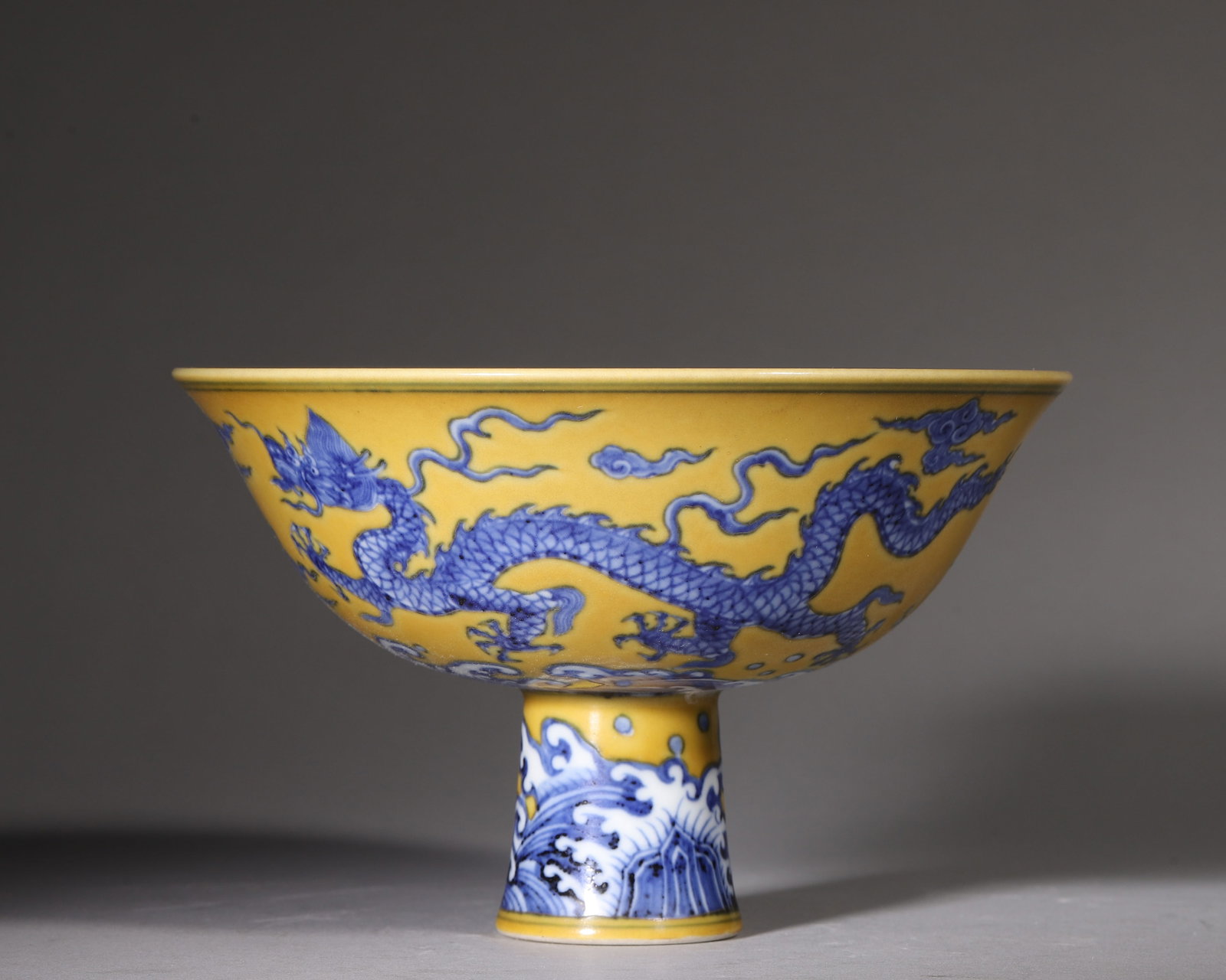 Yellow Ground Blueandwhite Stem Bowl With Dragon Cloud And Sea Wave Motifs, Xuande Ming (14261435: W 17cm (6.69 in); H 11cm (4.33 in)Stem bowl with overall yellow ground. Exterior painted in blueandwhite with dragon chasing pearl amid clouds. Stem decorated with searock patterns. Sixcharacter Xuand