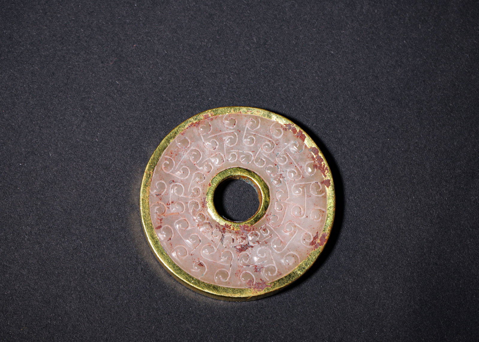Hetian Jade Bi Disc With Gilded Copper Mount And Grain Pattern, Han Dynasty (202 Bc 220 Ad): Wt 30g (0.066 lb); D 5.3cm (2.087 in)Carved from Hetian white jade in canonical bi disc form, inner and outer rims clad in gilded copper. The surface fully adorned with neatly arranged shallow relief 