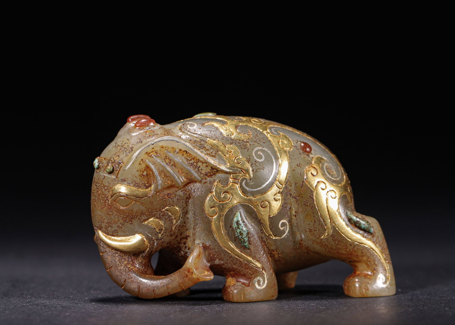 Gold And Silver Painted, Gemstone Inlaid Hetian Jade Elephant, Han Dynasty (202 Bc 220 Ad): Wt 151g (0.33 lb); L 7cm (2.76 in); W 3cm (1.18 in); H 4cm (1.57 in)Carved from pale Hetian jade as a standing elephant with coiled trunk. The surface is adorned with gold and silver painted scroll pa