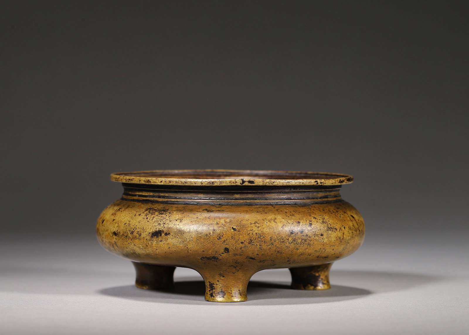 Bronze Tripod Censer, Xuande Mark (Ming Dynasty,1368 1644): Wt 484g (1.067 lb); D 9.5cm (3.74 in); H 4cm (1.57 in)Bronze censer with flared rim, string patterns at neck, full rounded belly and three bulbous feet. Mottled aged patina inside and out. Square fram