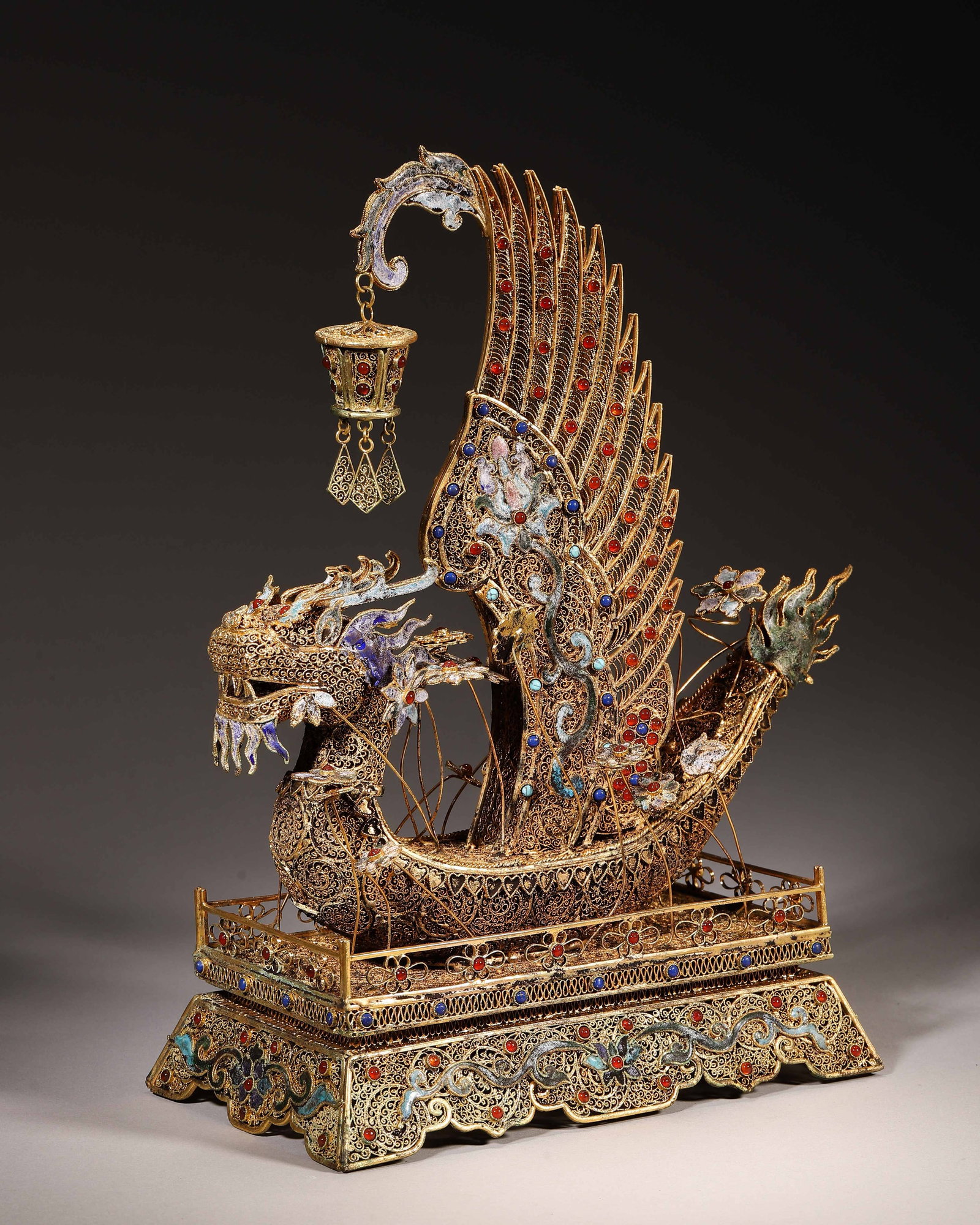 Gilt Copper Filigree Enamel Jewelled Dragon Boat, Qianlong Period Qing (1736 1795): Wt 1286g (2.84 lb); L 21cm (8.27 in); W 12cm (4.72 in); H 30cm (11.81 in)Gilt copper filigree dragon boat ornament with enamel and gem inlay. Hanging filigree lantern, two tier base, bears Qianlong ma