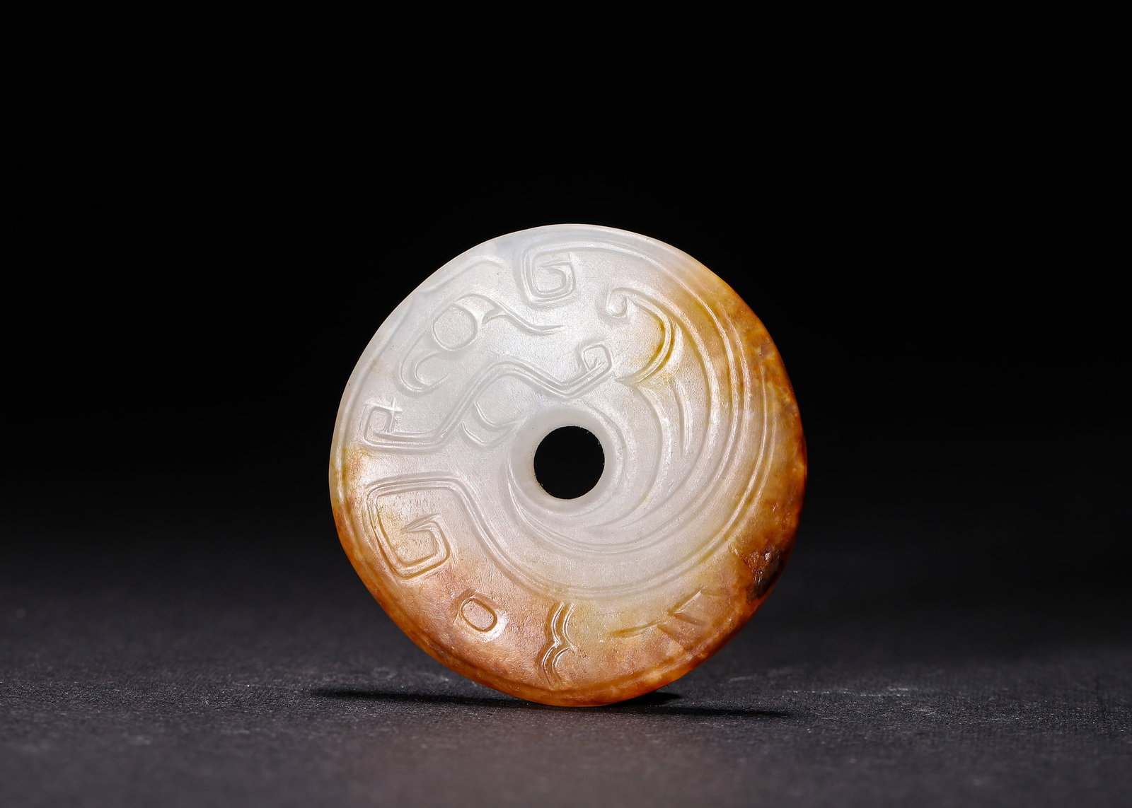 Hetian White Jade Bi Disc With Russet Skin And Phoenix Motif, Western Zhou Dynasty: D 5cm (1.97 in)Carved from Hetian white jade with natural russet skin. This circular bi disc has central aperture, incised phoenix and spiral patterns, serving as ritual jade ornament of Western Zhou 