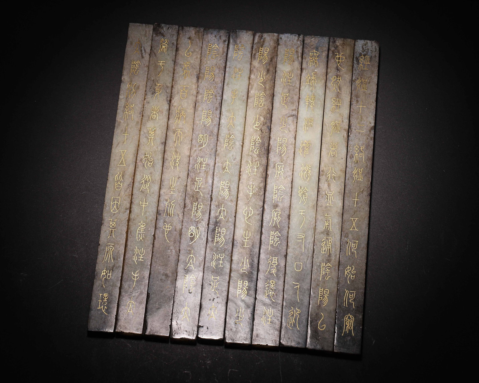 Set Of Ten Hetian Jade Slips With Gilded Inscriptions, Han Dynasty (202 Bce 220 Ce): Wt 883g (1.95 lb); L 25cm (9.84 in); W 1.8cm (0.71 in)A set of ten rectangular Hetian Jade slips. The jade shows varied grey brown and dark brown patina. Obverse sides bear seal script characters with