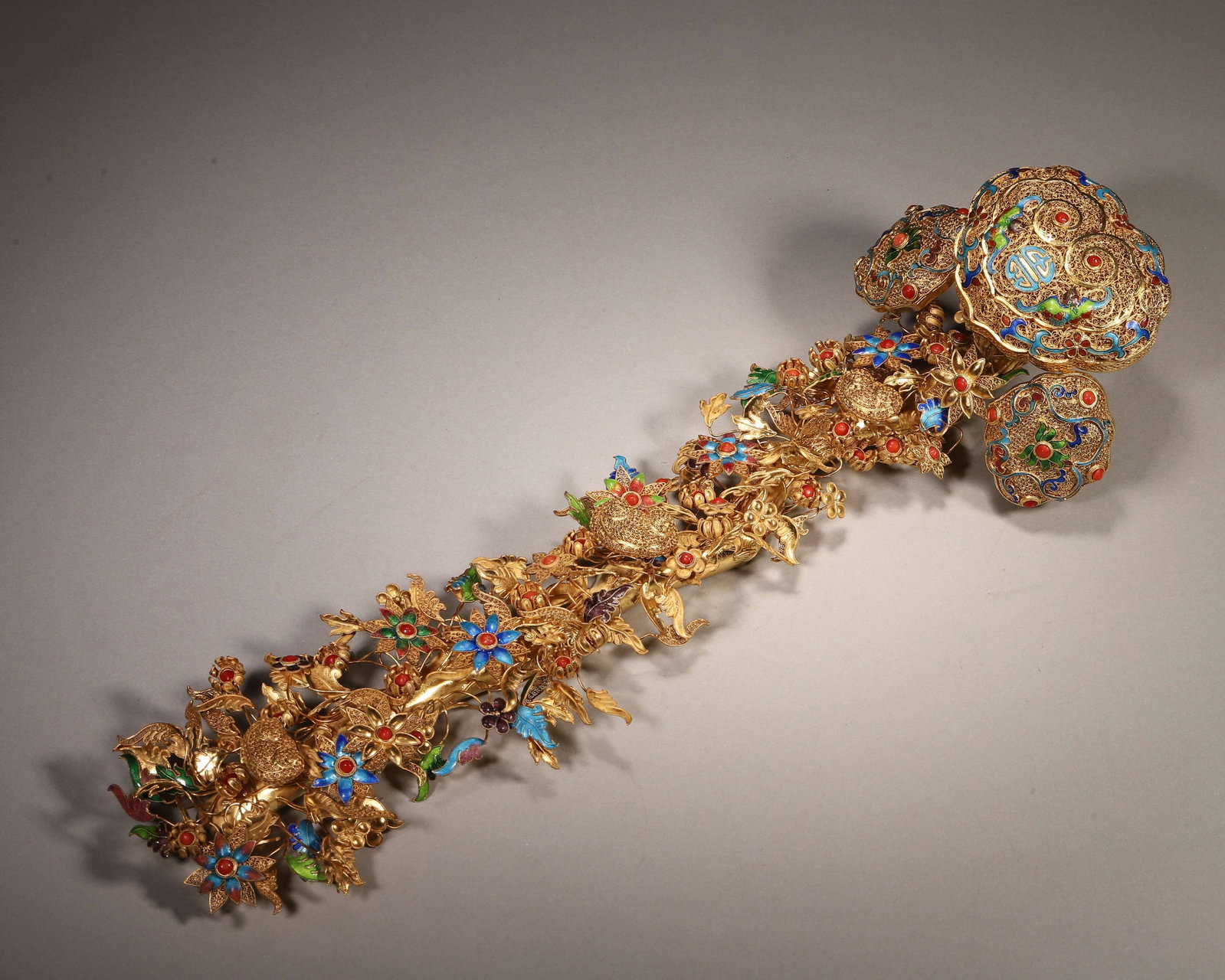 Gilt Copper Filigree Enamel Inlaid Ruyi Scepter Qing Dynasty: Wt 535g (1.18 lb); L 39cm (15.35 in); W 11cm (4.33 in)Gilt copper ruyi scepter with fine filigree work. Enamel and gem inlay decorate lingzhi head. Stem adorned with floral and fruit motifs, imitating