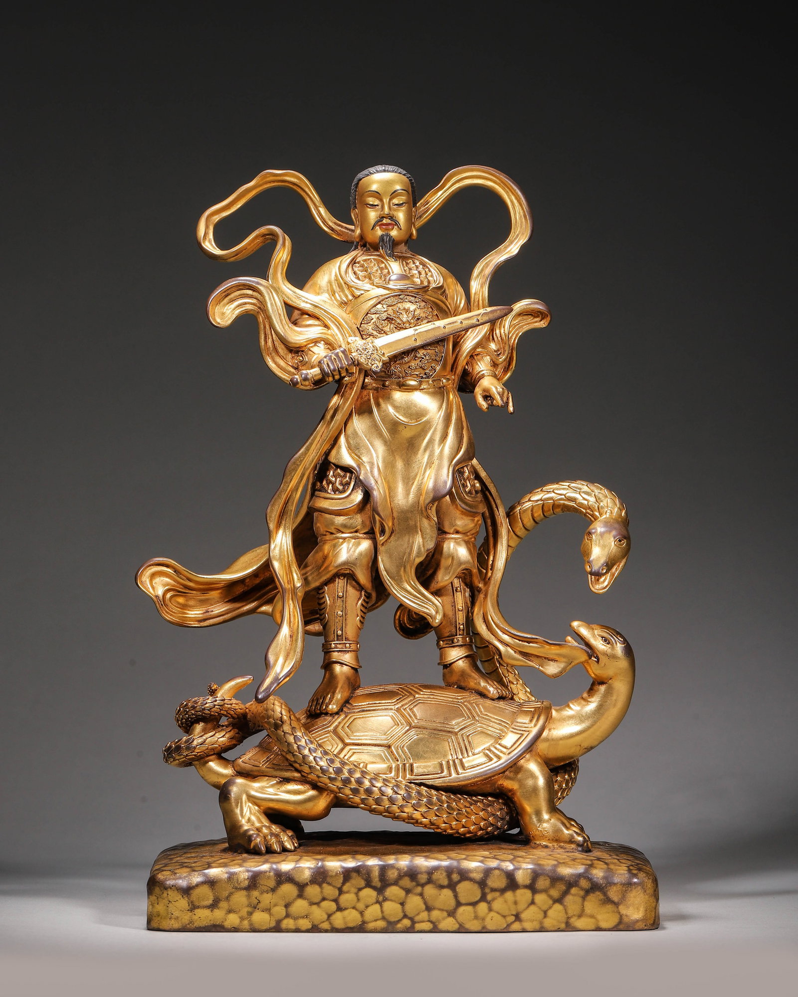 Gilt Bronze Standing Statue Of Emperor Zhenwu,Qing Dynasty: Wt 3953g (8.71 lb),L 18cm (7.087 in),W 13cm (5.12 in),H 28cm (11.024 in)Imperial court made.Emperor Zhenwu stands atop the Xuanwu tortoise and serpent on a square rock textured plinth. He has a serene