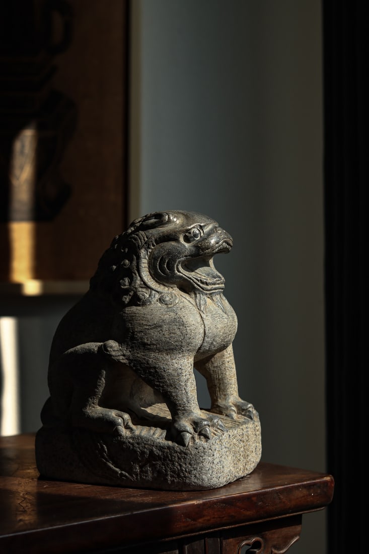 Bluestone Seated Lion Figure, Qing Dynasty (1644 1912): H 25cm (9.84 in); L 18cm (7.087 in); W 14cm (5.51 in)Bluestone carved lion in squatting posture, with full spiral mane, open mouthed detail and square base. Weathered surface, simple and robust carvin