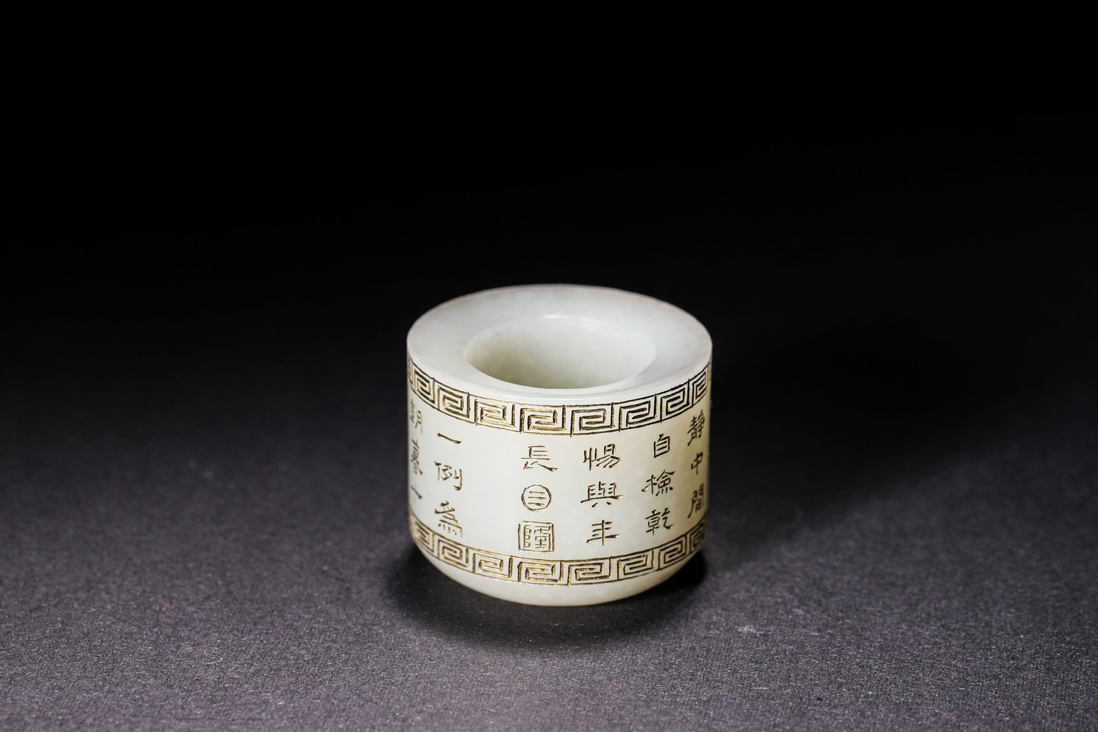 Hetian White Jade Thumb Ring, Qing Dynasty (1644 1912): Wt 52g (0.11 lb); Inner D 2.2cm (0.87 in); W 2.9cm (1.14 in)Cylindrical thumb ring of Hetian white jade. Borders carved with key fret pattern. Imperial poems incised and gilt filled on surface, with i