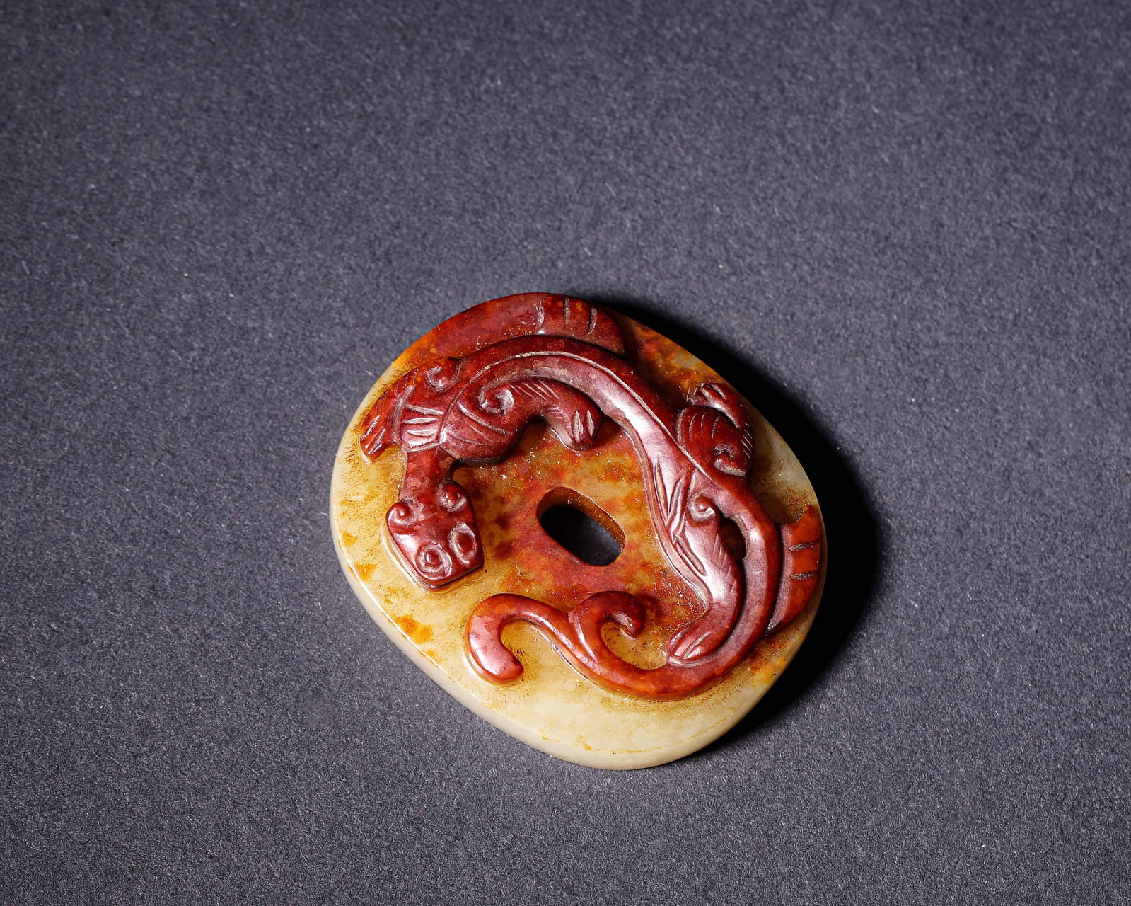 Nephrite Disc With High Relief Chilong And Red Russet, Han Dynasty (202?Bce 220?Ce): Wt 30g (0.066 lb); L 4.2cm (1.65 in); W 3.5cm (1.38 in)Oval nephrite disc with deep red russet. One side high relief chilong carving, reverse incised cloud and grain motifs, oval central aperture, anc
