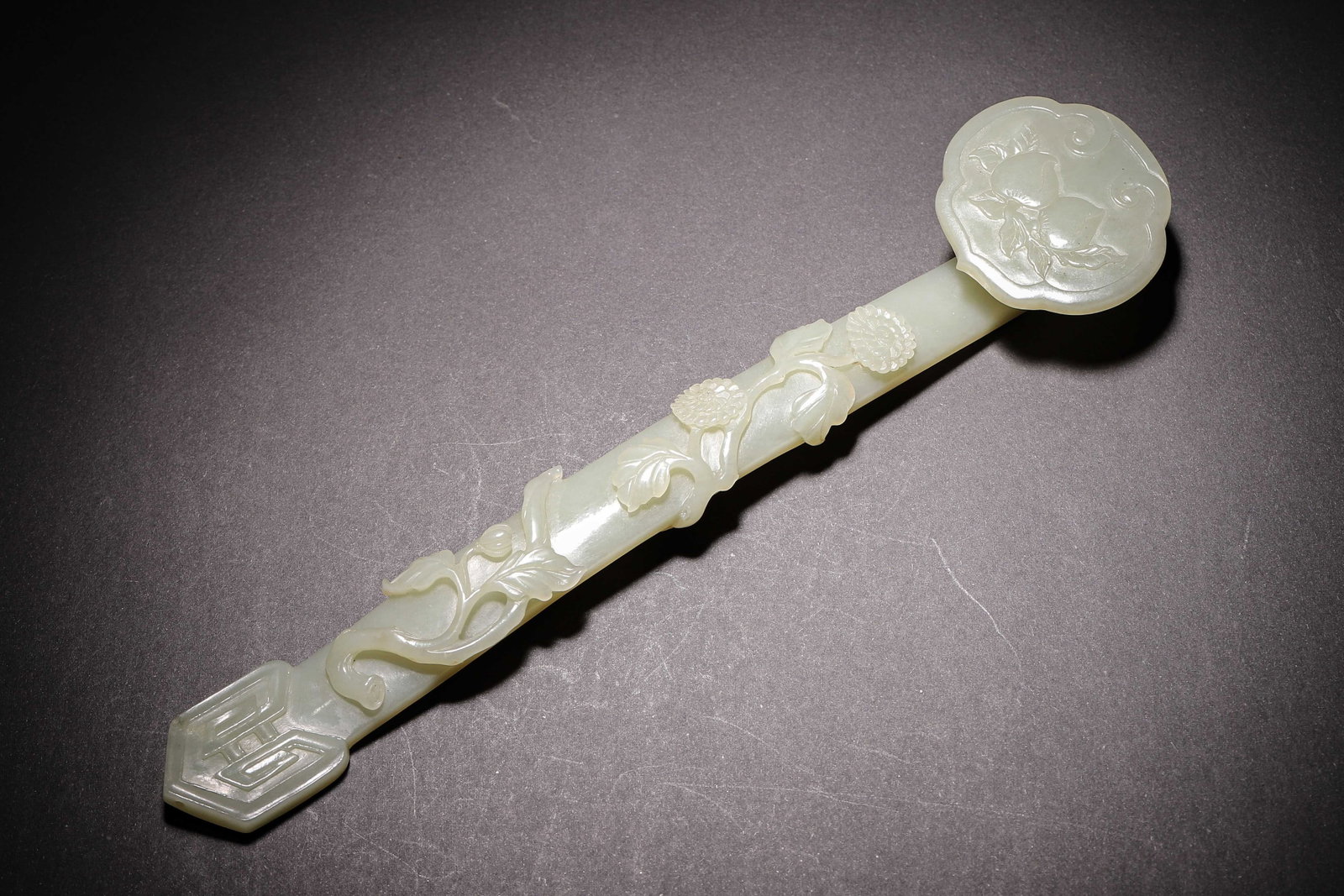 Nephrite Ruyi With Relief Peach And Chrysanthemum Decoration, Qing Dynasty (1644 1912?Ce): Wt 162g (0.36 lb); L 25cm (9.84 in); W 5.5cm (2.17 in)Celadon nephrite ruyi. Ruyi head carved with peaches, shaft decorated with raised chrysanthemum branches, terminal with archaic scroll pattern, fi