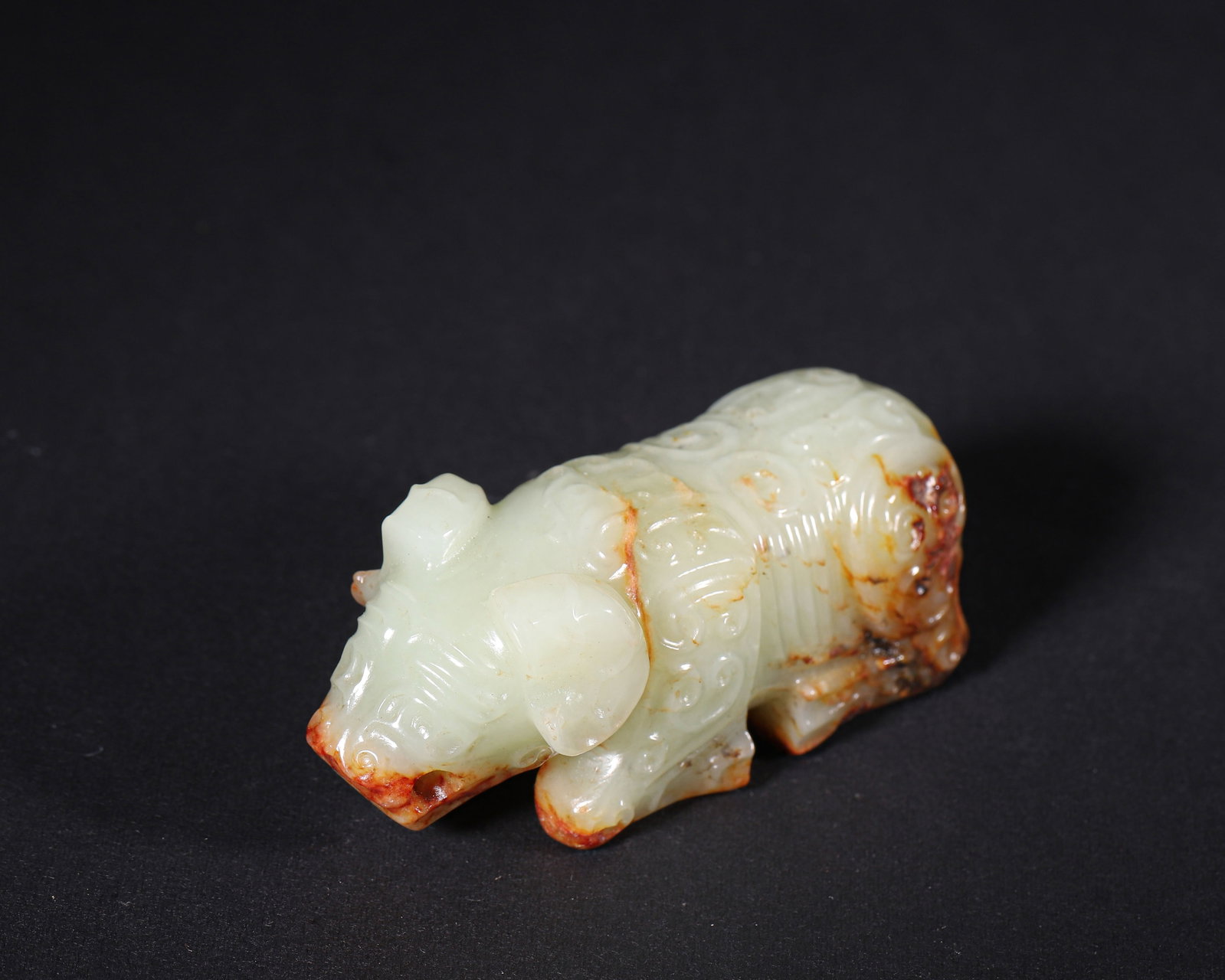 Celadon Hetian Jade Recumbent Beast Toggle,Zhou Dynasty(1046 256 Bc): Wt 129g (0.28 lb); L 7.8cm (3.071 in); W 3cm (1.18 in); H 3.2cm (1.26 in)Celadon Hetian jade recumbent beast toggle with reddish brown inclusions. Decorated with scrolling cloud patterns, pierced at s