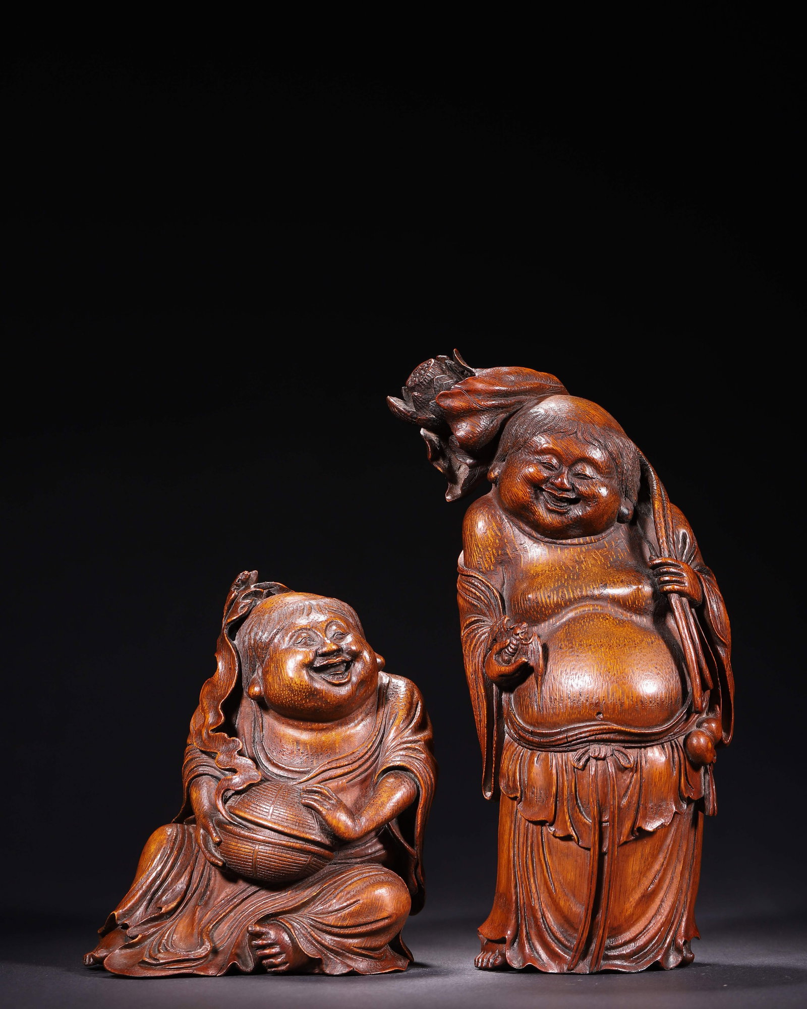 A Pair Of Bamboo Carved He He Immortals, Qing Dynasty, 1644 1912A.D.: Wt 1164g (2.57 lb); L 11cm (4.33 in); W 8cm (3.15 in); H 24cm (9.45 in)Bamboo root carving,one standing,one seated. Standing figure carries lotus over shoulder,holds ritual object with flowing robe. S
