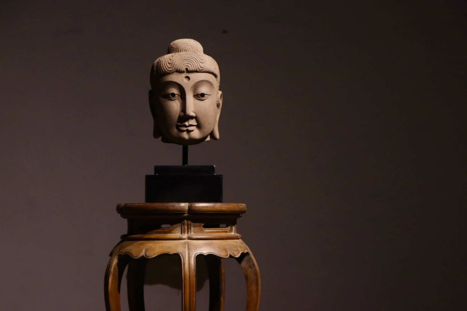 Stone Carved Buddha Head, Northern Wei Dynasty (386 534): H 33cm (12.99 in); L 21cm (8.27 in); W 22cm (8.66 in); Overall H 52cm (20.47 in)Sandstone Buddha head with wavy spiral hair and rounded ushnisha. Urna on forehead, elongated ears, serene facial expres