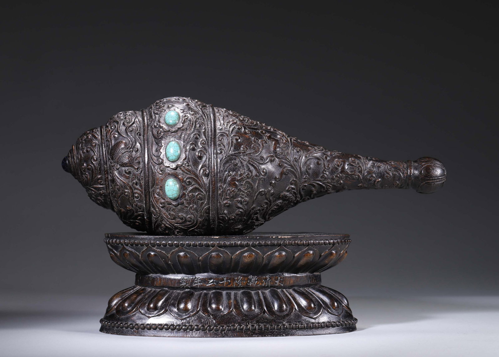 Qing Dynasty,Chenxiang Carved Dharma Conch With Interlocking Floral And Eight Auspicious Symbols: Carved from solid chenxiang agarwood in the form of a dharma conch, densely decorated with interlocking floral and eight auspicious emblems and inlaid with turquoise. The tip is finished with a pearl 