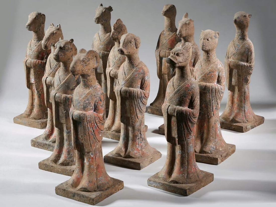 Tang Dynasty, A Group Of Painted Limestone Zodiac Figures: Painted limestone for tomb burial. Set of twelve animal-headed human figures in cross-collared robes, hands folded on chest, square bases. Remnants of red and blue pigments, soil erosion and weatherin