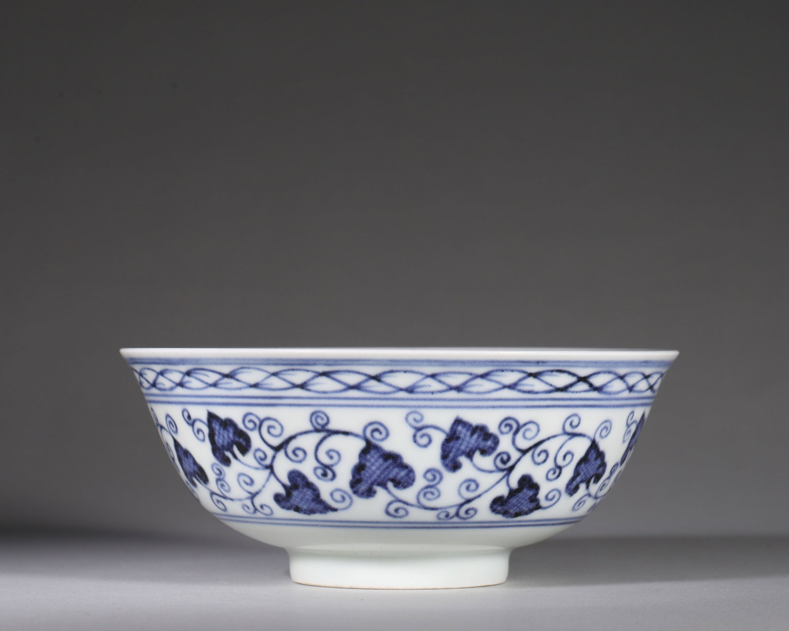Blue And White Bowl With Interlocking Floral Scrolls, Xuande Period Ming Dynasty (14261435 Ce): Widemouthed bowl with curved wall and ring foot. Rim decorated with twistedrope pattern. Exterior painted with blue and white interlocking floral scrolls. Interior fully decorated with diaper ground a