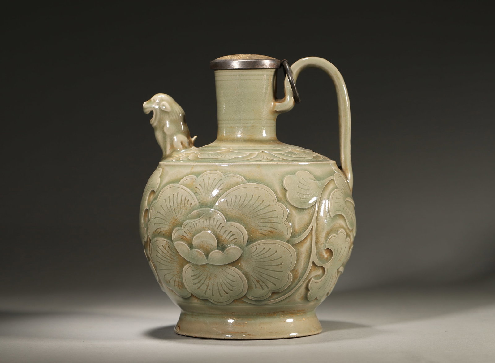 Celadon Ewer With Carved Peony And Lion Spout,Song Dynasty,960-1279: Straight neck,bulbous body and ring foot,lion-form spout and curved handle,metal mounted cover.Carved peony scrolls on body with distinct layers,covered in smooth celadon glaze.D 16cm (6.299 in); H 21