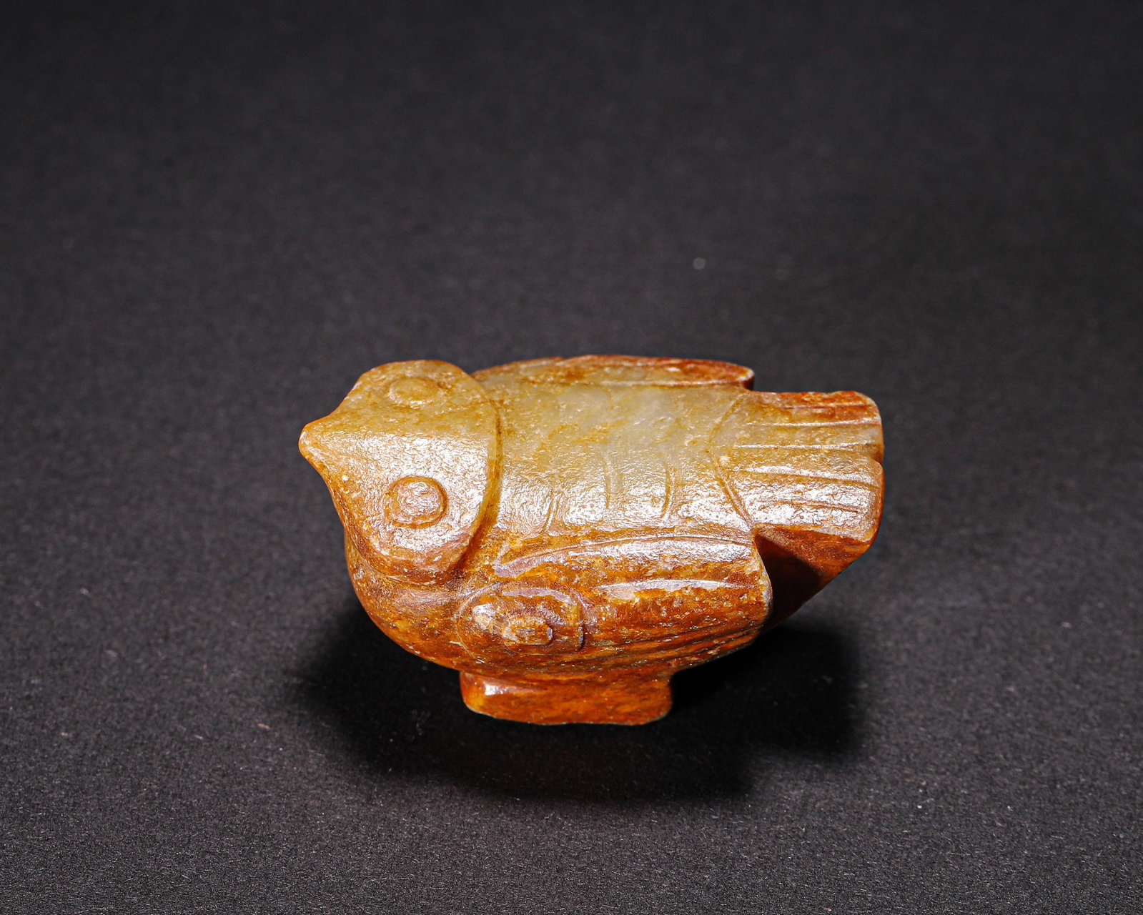 Jade Bird-Shaped Pendant,Shang Dynasty (1600 Bc-1046 Bc): The jade is stained with yellow-brown patina.Part retains original jade colour.Round carved bird form.Relief and incised lines depict eyes,wings and tail.A perforated base for suspension.Typical shang