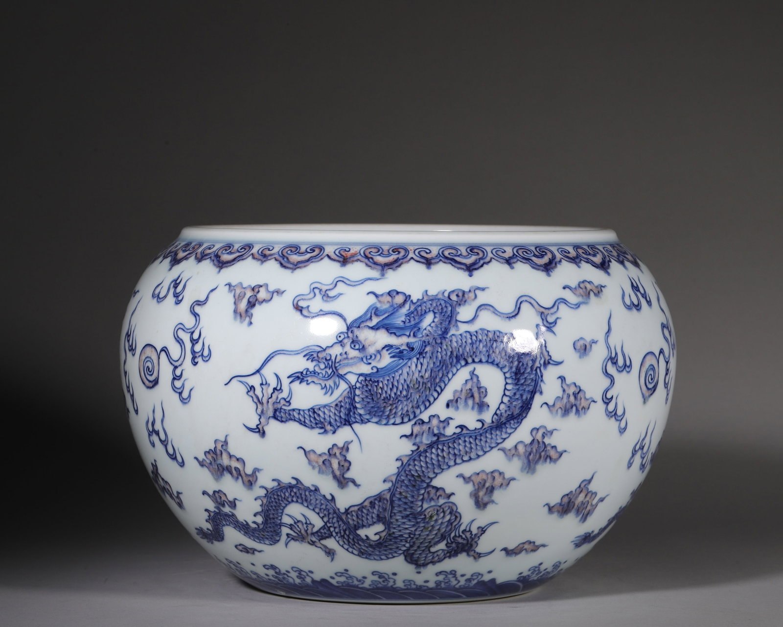 Blue And White Dragon Cloud Almsbowl Shaped Jar, Kangxi Period Qing Dynasty (16621722 Ce): Almsbowl form with contracted mouth, bulging belly and ring foot. Exterior painted with fiveclawed dragons amid clouds and flames. Ruyi scrolls at rim, seawave pattern near base. Sixcharacter Kangxi