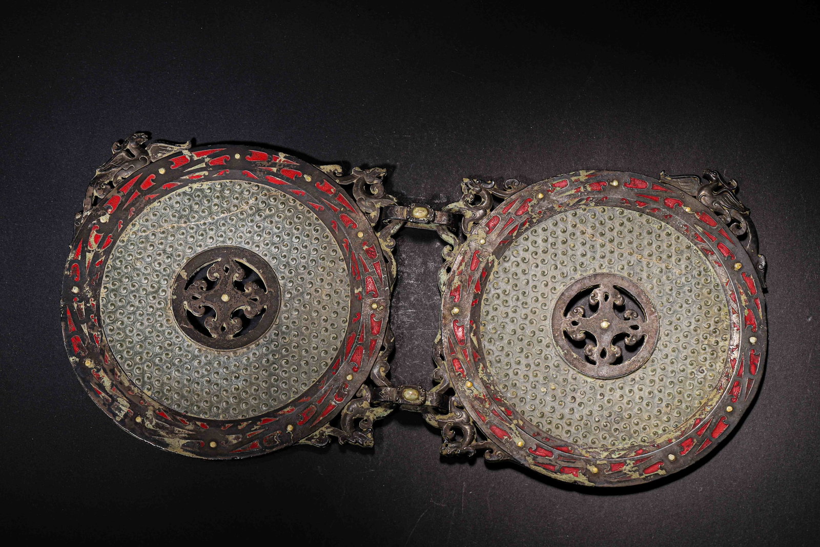 Bronze Linked Bi Discs With Red Lacquer Inlay, Warring States Period, 475 221 B.C.: A pair of linked bi discs joined by openwork dragon form hinge. Surface fully covered with grain pattern, with open floral aperture at centre. Outer rim carved with dragon and phoenix openwork, inlaid