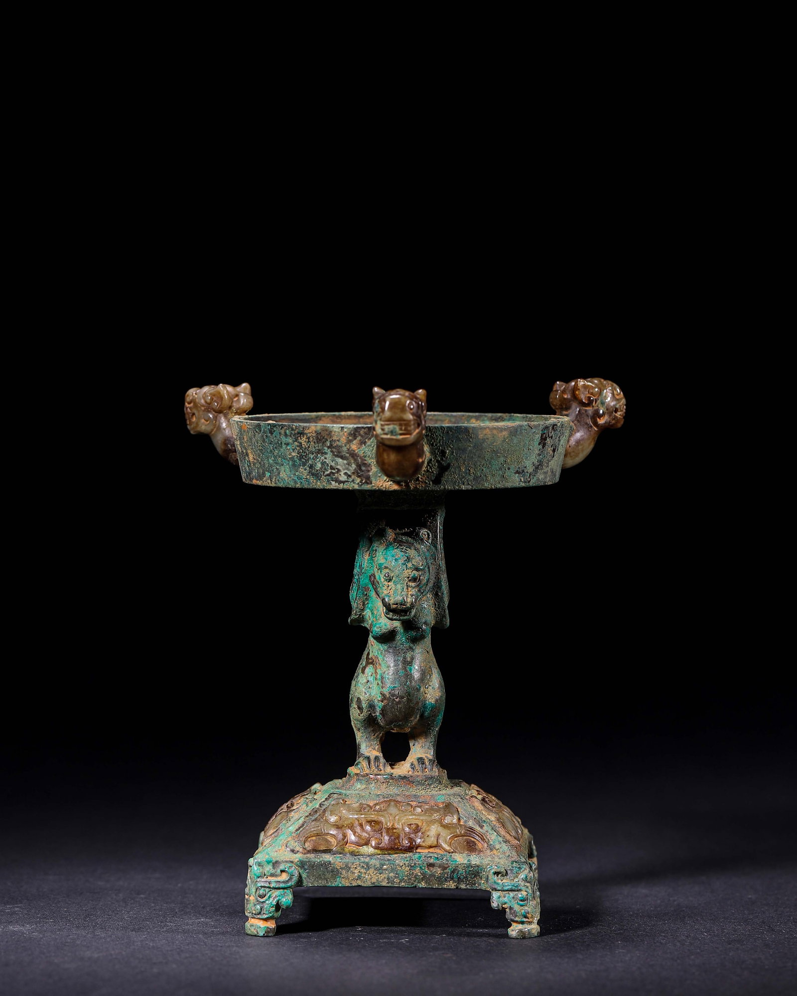 Han Dynasty,Bronze Lamp Supported By Bear With Three Jade Beast Heads: This is a Han Dynasty bronze lamp with a square four-legged base inlaid with jade beast-mask patterns. A standing bear serves as the supporting pillar. Three jade beast heads extend outward from the e