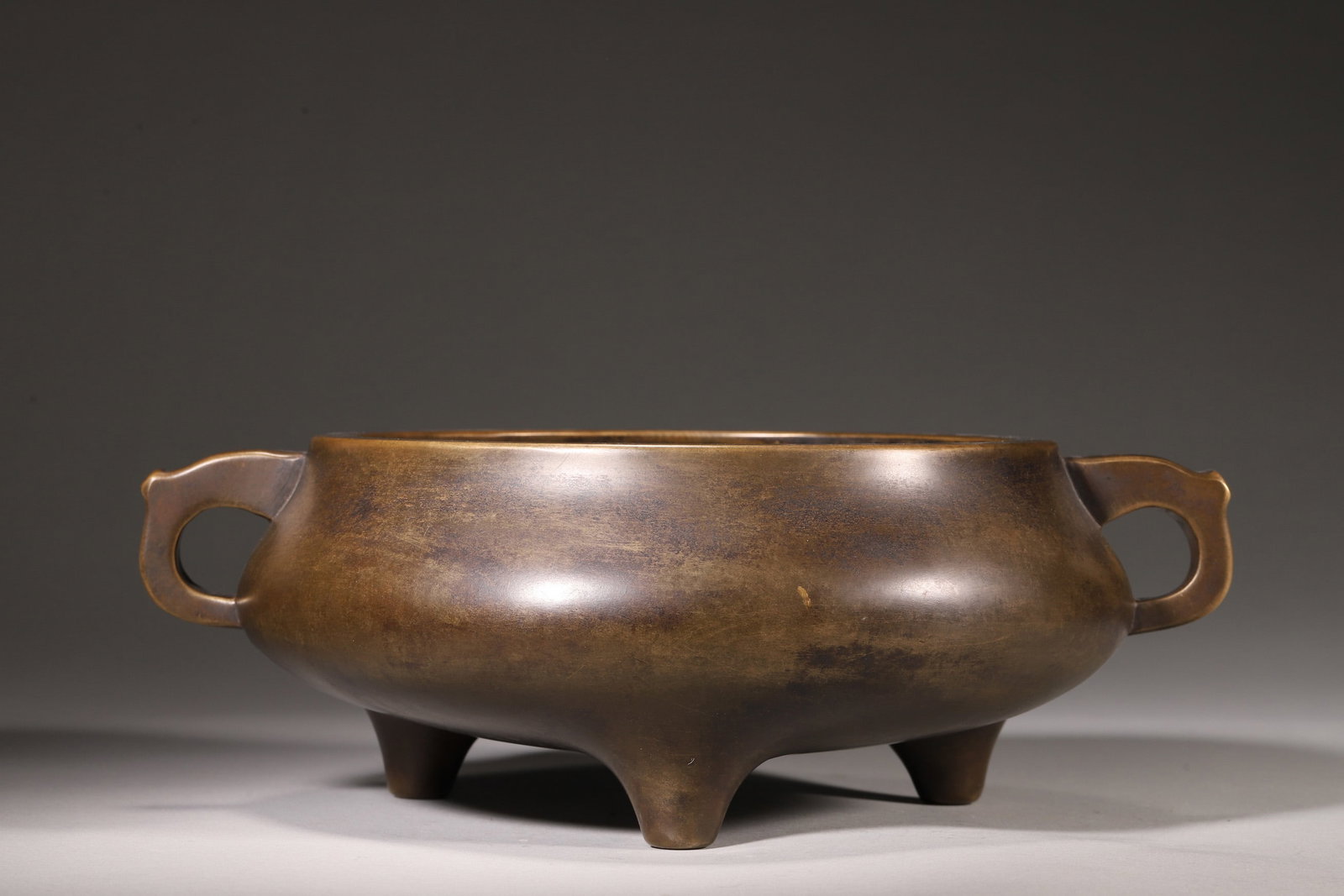 Ming Dynasty Bronze Three-Foot Censer With Pan Handles, "Xuande Nian Zhi" Mark: A bronze three-foot censer with pan handles, bearing the "Xuande Nian Zhi" mark, dating to the Ming Dynasty. Cast from refined bronze, it features a warm chestnut patina with mellow luster. The rounde