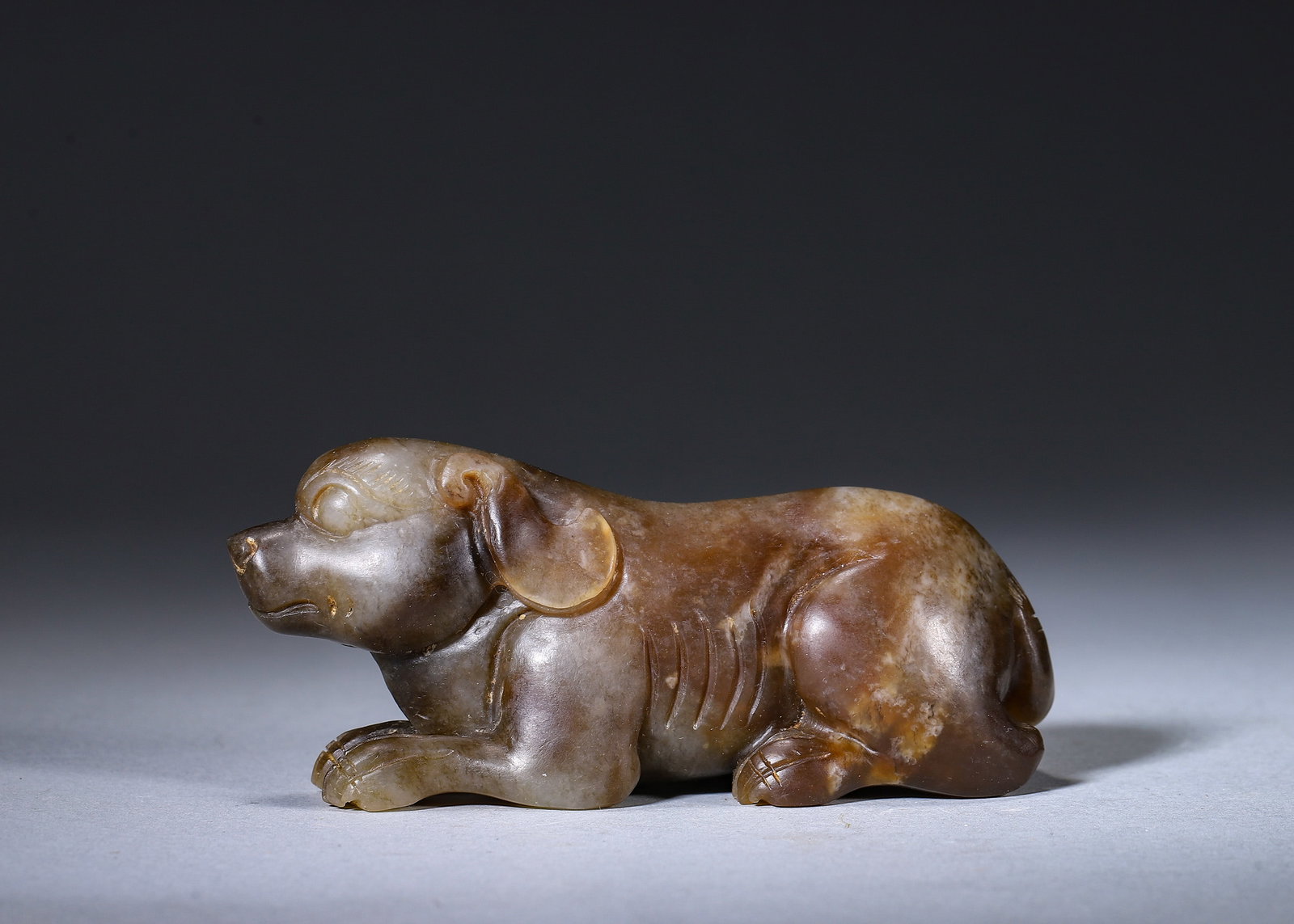 Yuan Dynasty, Recumbent Jade Dog: L:10cm W:3.5cm H:4.5cm WT:222g(L:3.94in W:1.38in H:1.77in WT:0.49lb)This recumbent dog is carved from Hetian jade. It lies prone with head turned forward, drooping ears and coiled tail, featuring a st