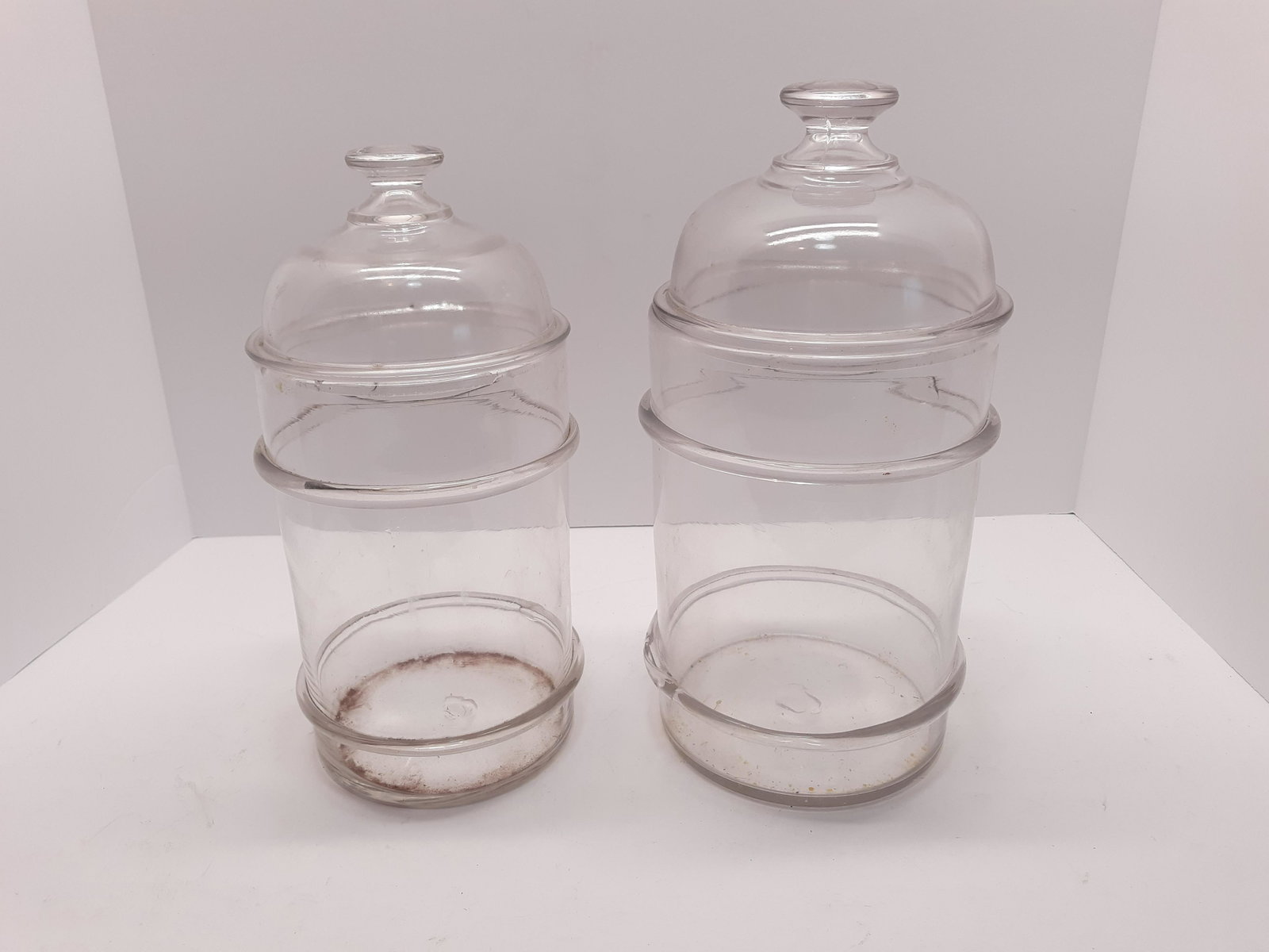 Two Hand Blown Cracker Jars: 2 hand blown display or cracker jars. Bead ridges around the exterior of the jars has been hand applied. One jar is chipped on the lip and the lid. 11 1/2" & 12 1/2"