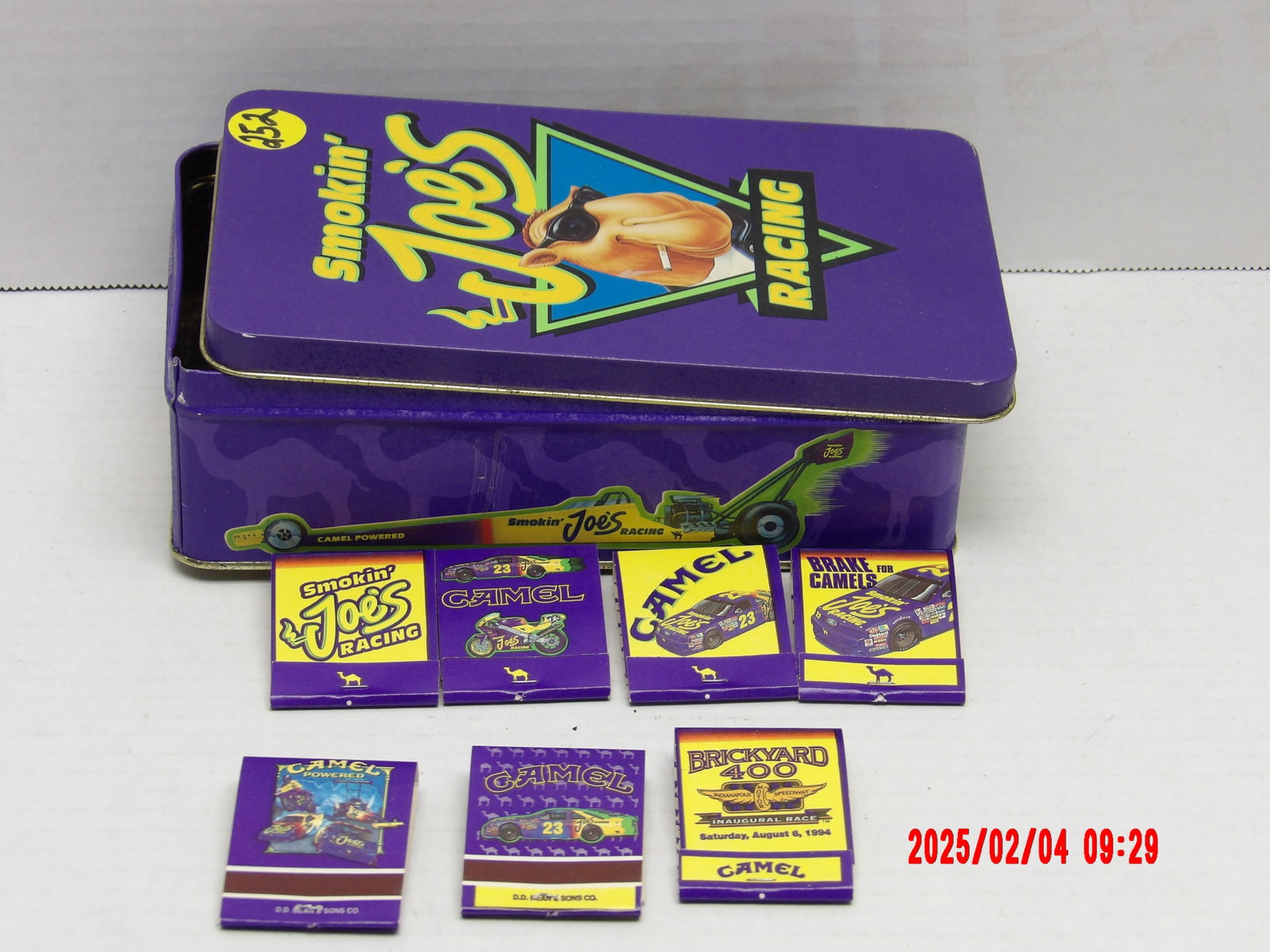 Smokin' Joe's Racing Collectible Tin & Camel Matchbooks: This lot showcases a Smokin’ Joe’s Racing collectible tin, along with six vintage Camel-branded racing matchbooks. The items commemorate Camel’s sponsorship of NASCAR and motorsports, particular