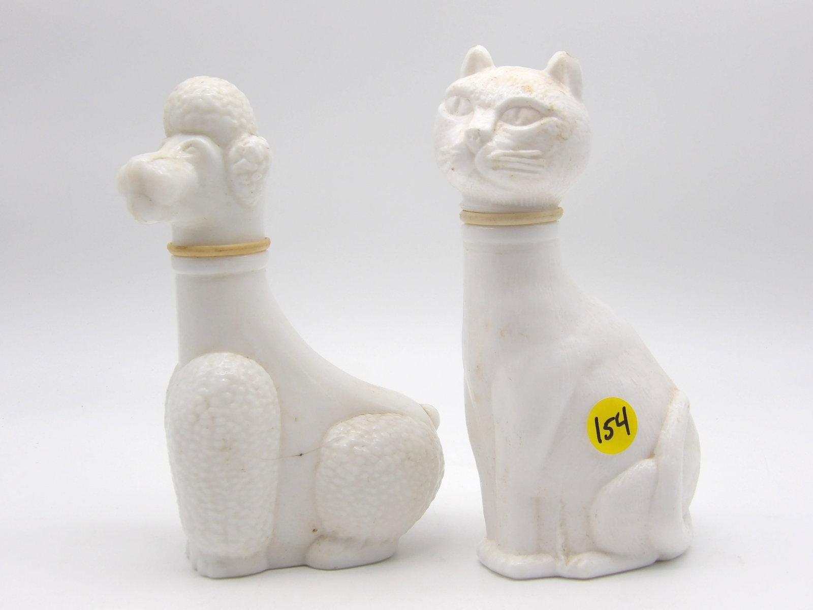 AVON DOG & CAT BOTTLES (PAIR): These ‘milk glass’ style figure bottles were made by AVON and are highly collectible with fans of vintage glass, bottles, and Avon products. (7” X 4”)