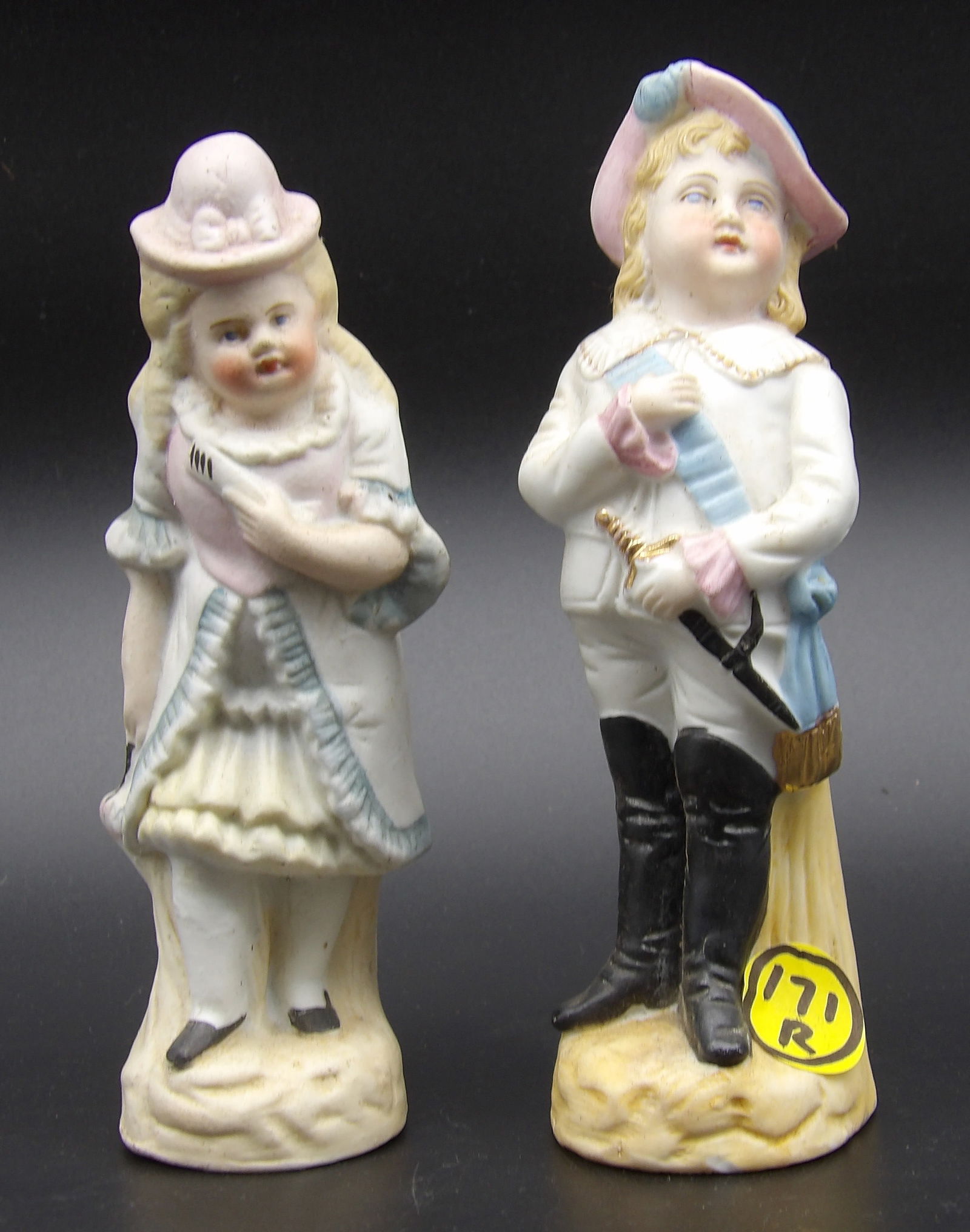 BISQUE PORCELAIN FIGURINE PAIR: This pair of bisque porcelain figurines features a boy and girl in fancy dress