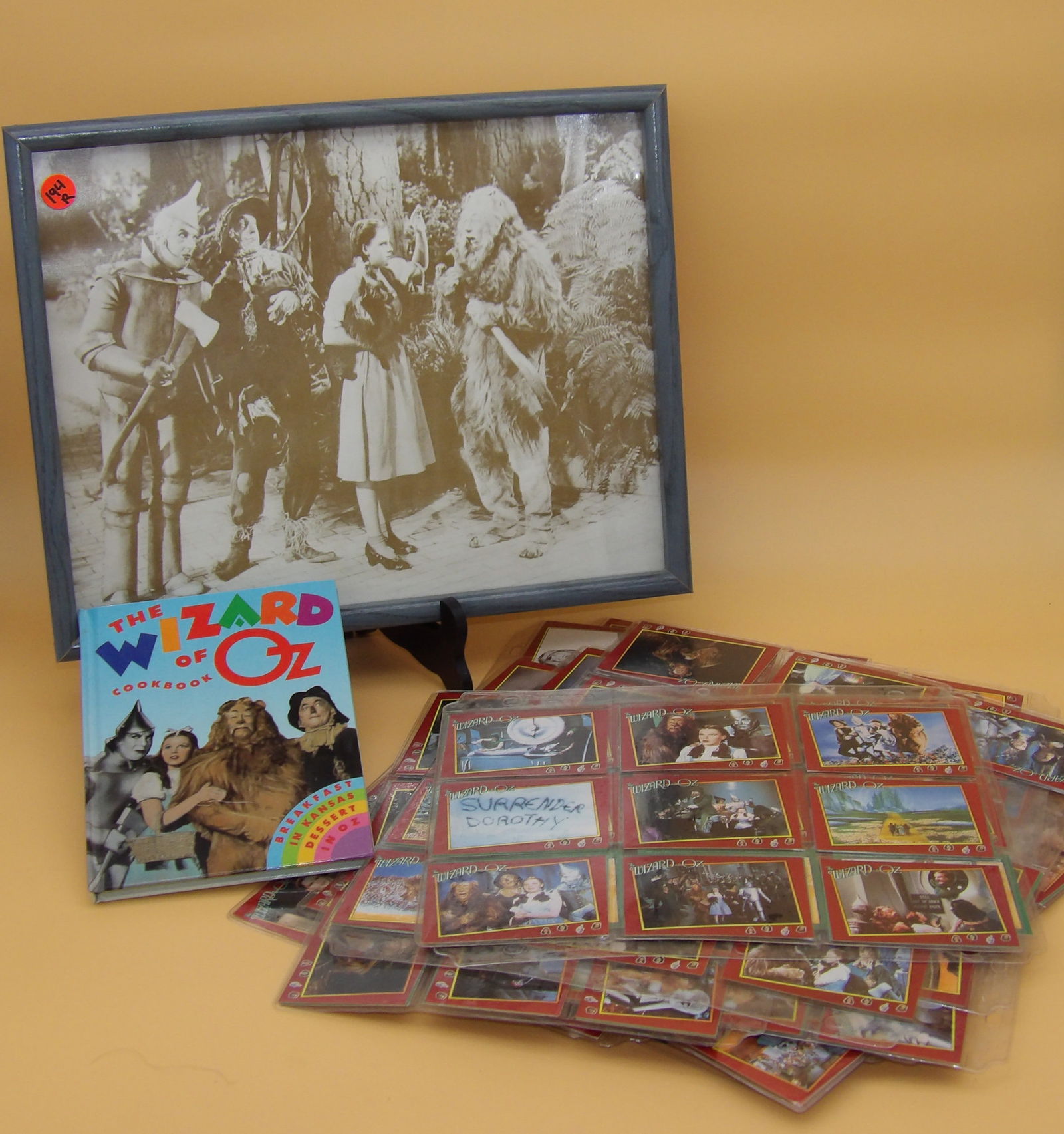 Wizard of Oz Framed Photo, Trading Cards, and Cook Book: This Wizard of Oz lot includes sleeved Trading Cards (Pacific Trading Cards Inc), a 'Wizard of Oz Cookbook', and a framed photo from the film. Measures 14.5" x 12"